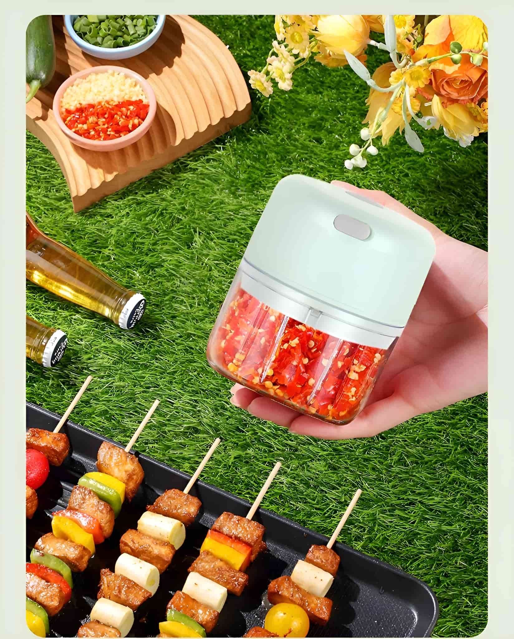 Eine Hand hält einen kleinen Zerkleinerer, gefüllt mit gehackten roten Paprika. Spieße mit gegrilltem Fleisch im Hintergrund.