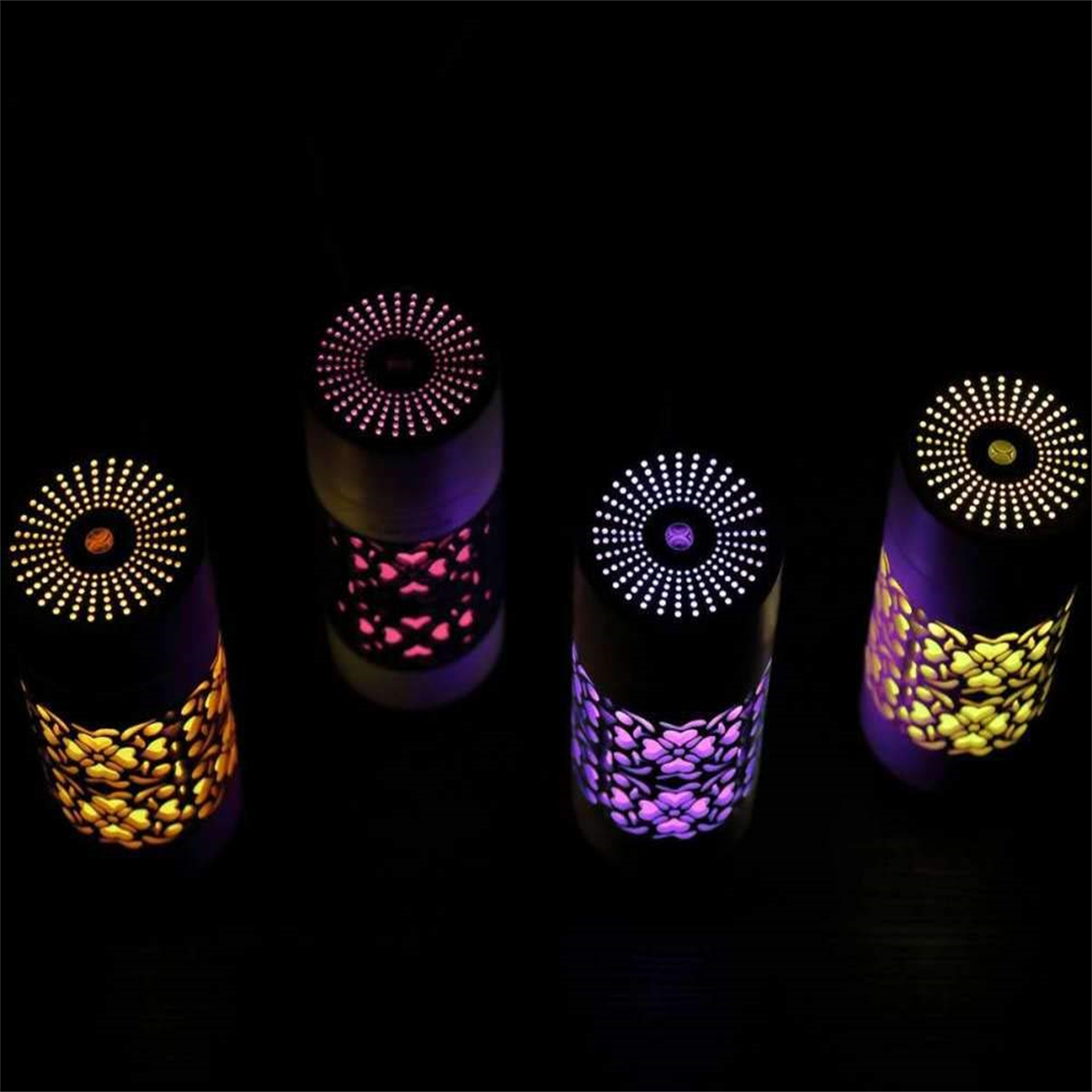Vier zylindrische Lampen mit leuchtenden Mustern. Die Lampen sind schwarz mit einem Design aus gelben und lila Lichtern.