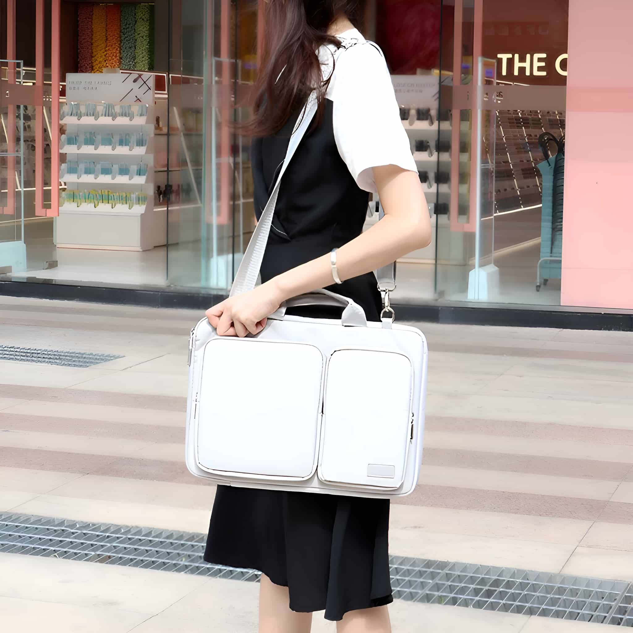 Frau trägt eine weiße Laptoptasche mit zwei Taschen. Der Hintergrund ist eine Geschäftsstraße.