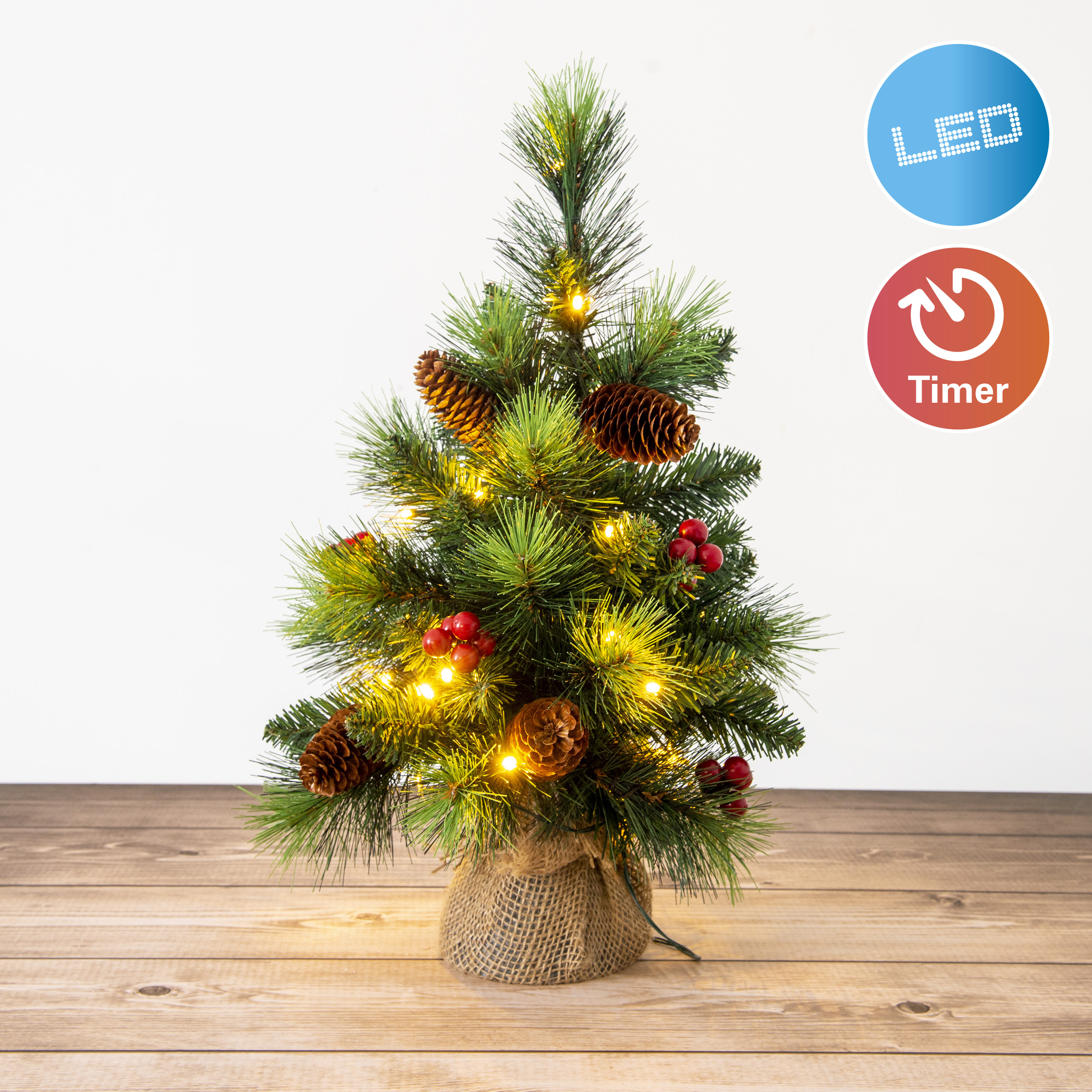 Kleiner künstlicher Weihnachtsbaum mit Lichtern, Tannenzapfen und roten Beeren, auf Holzoberfläche. LED- und Timer-Symbole.