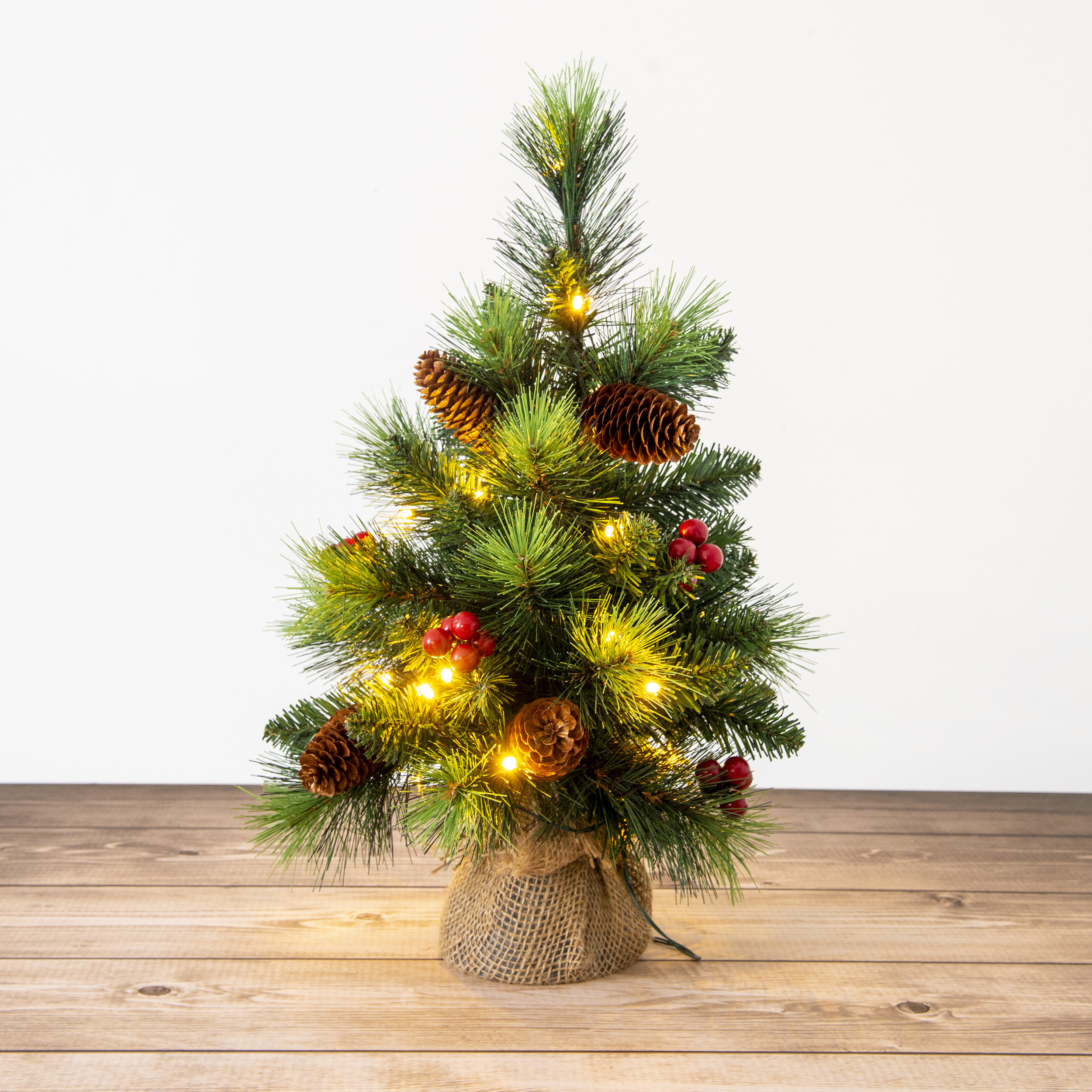 Ein kleiner künstlicher Weihnachtsbaum mit Lichtern und Tannenzapfen. Er steht auf einem Holztisch.