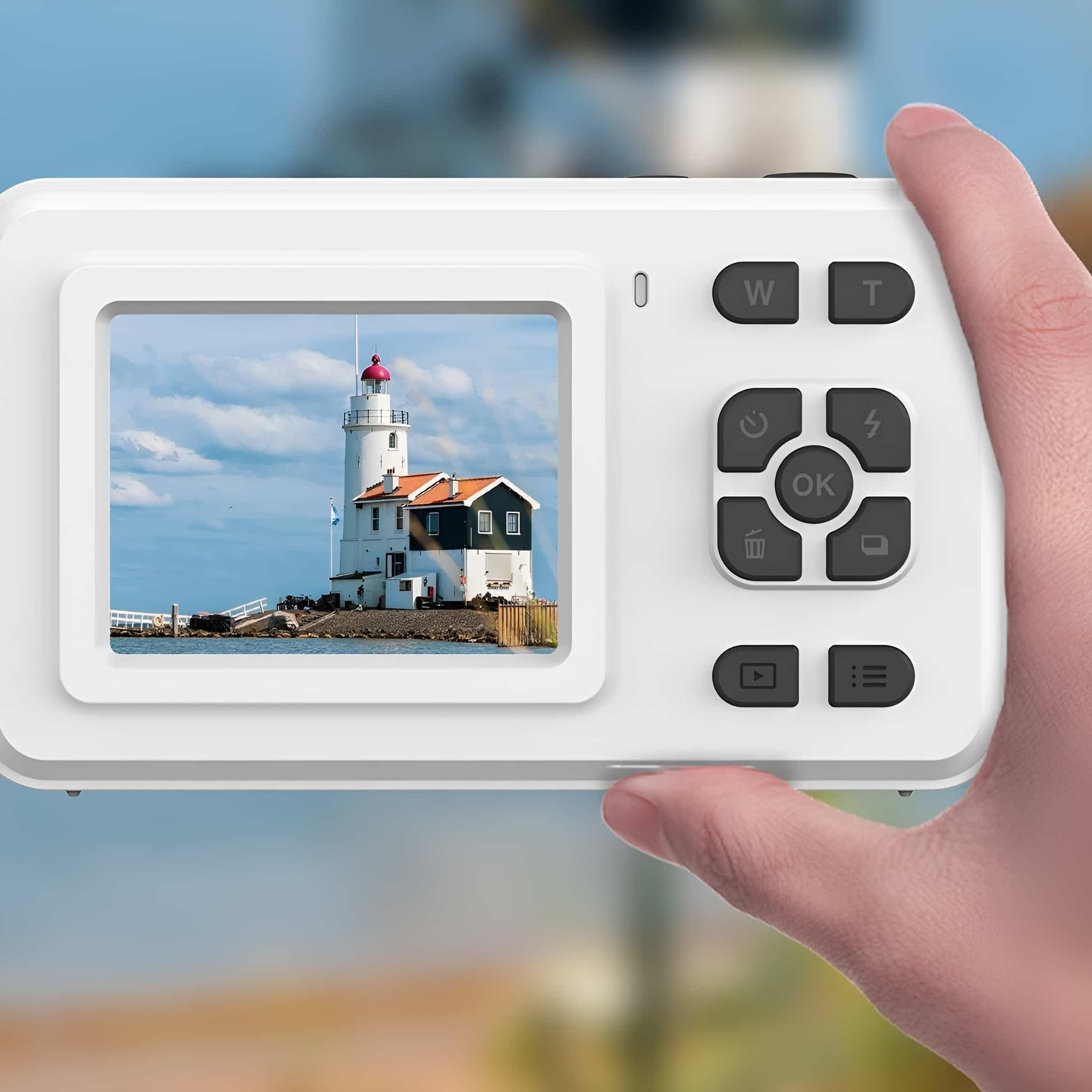 Weiße Digitalkamera mit Leuchtturmbild, gehalten von Hand vor unscharfem Hintergrund.