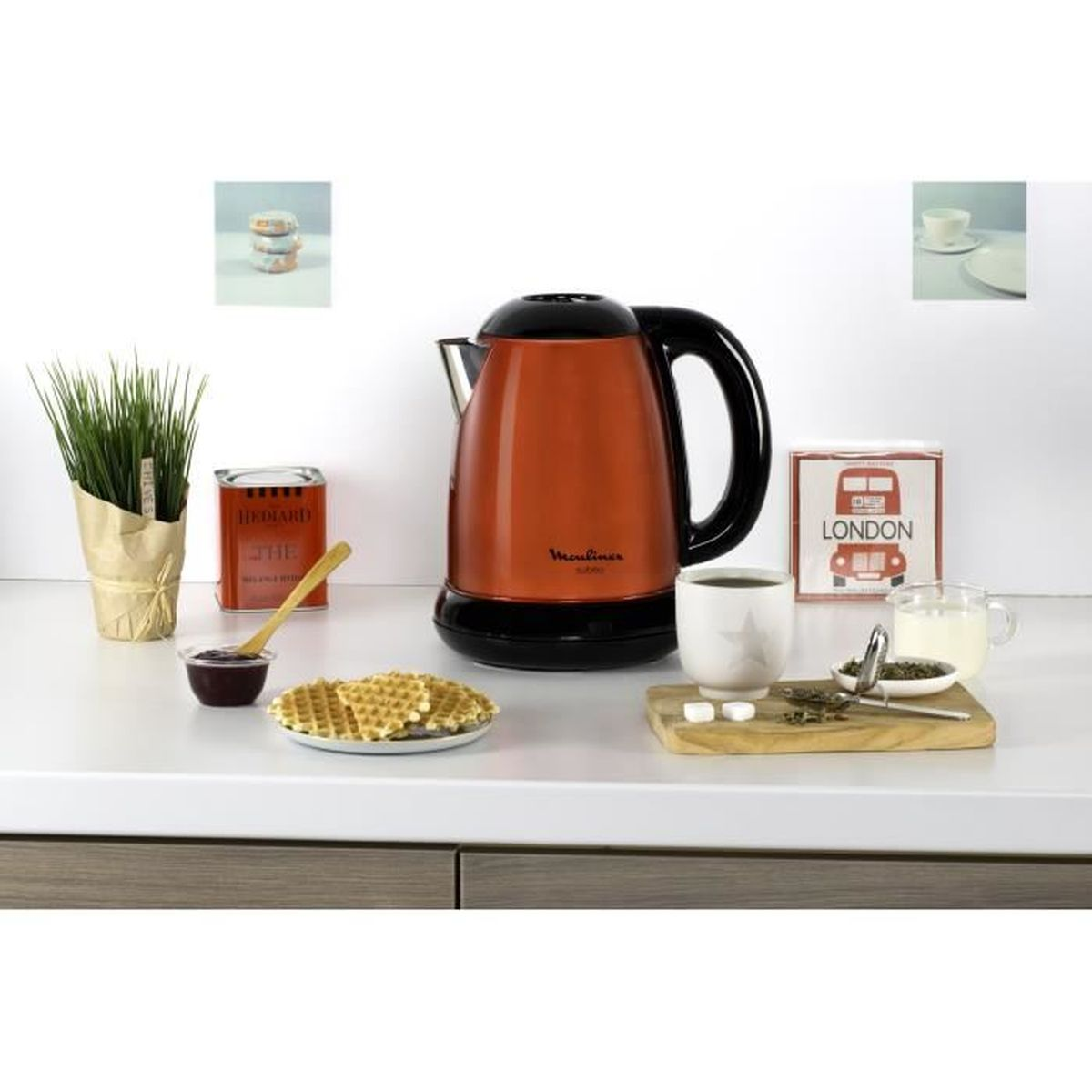 Czajnik, gofry, herbata i inne przedmioty kuchenne ułożone na białym blacie. Tło to kuchnia.