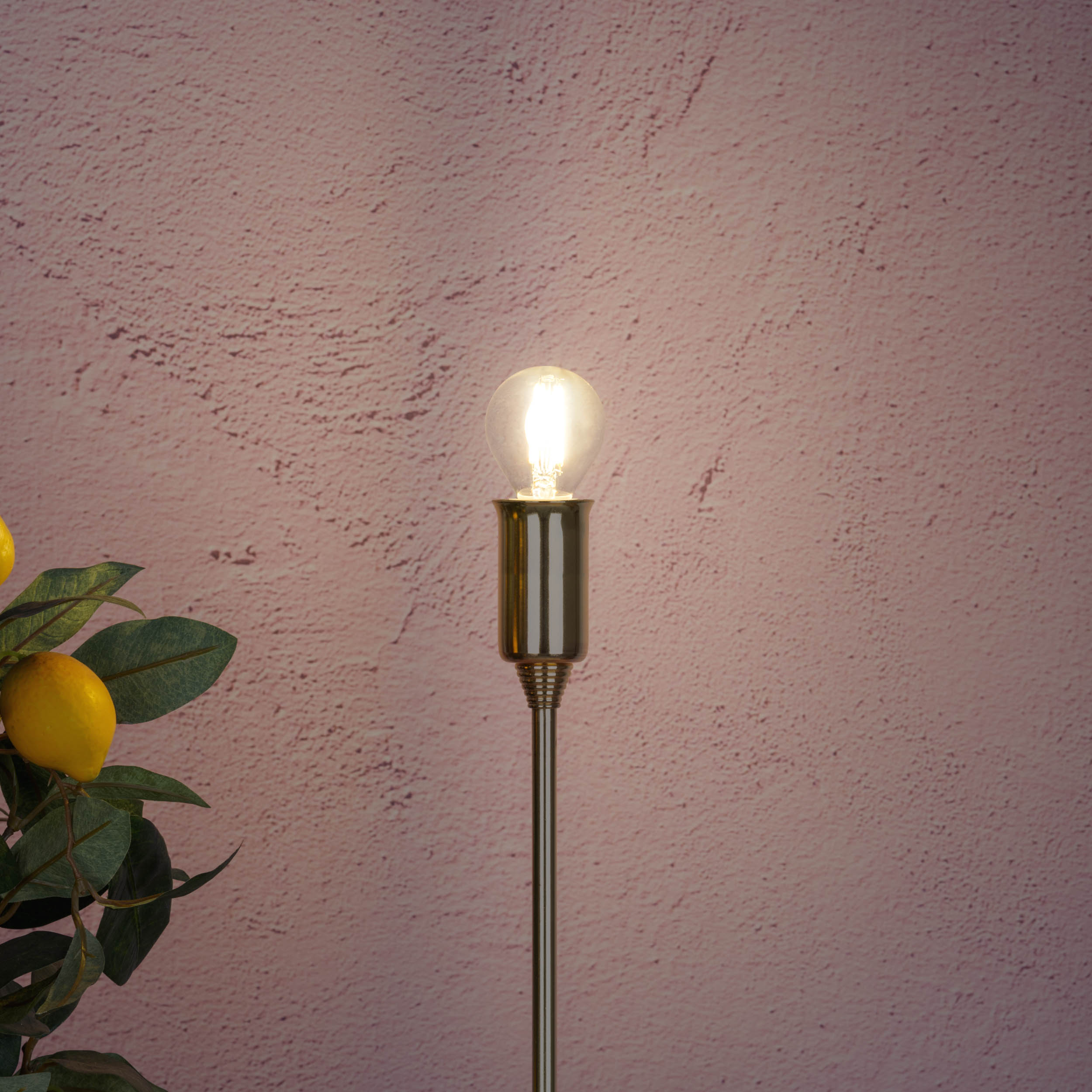 Eine leuchtende Glühbirne auf einem goldenen Stiel vor einer strukturierten rosa Wand.