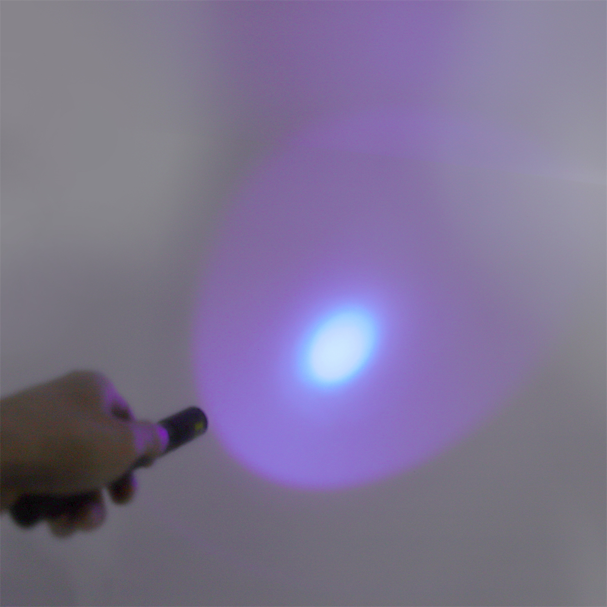 Eine Hand, die einen schwarzen Stift hält und ein helles lila Licht auf eine weiße Wand wirft. Ein helles Zentrum.