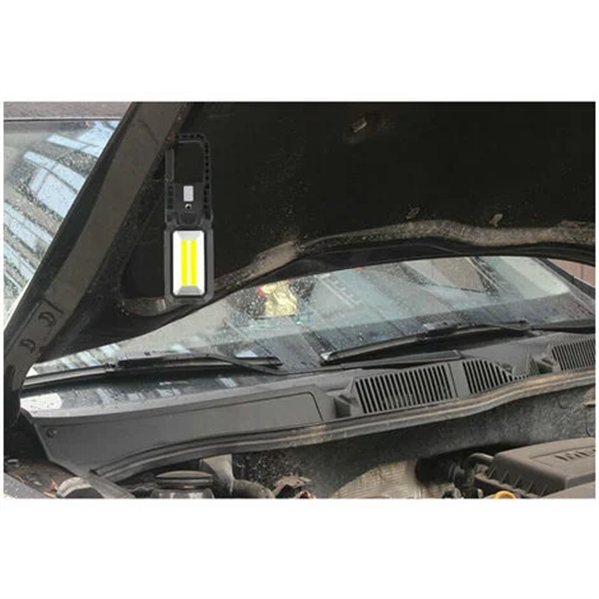 Eine schwarze Arbeitsleuchte, die unter einer Motorhaube hängt.