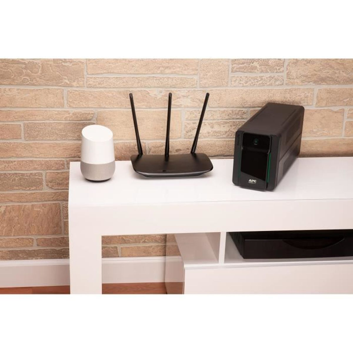 Weißer Tisch mit Smart Speaker, Router und APC Easy-UPS. Ziegelmauer im Hintergrund.