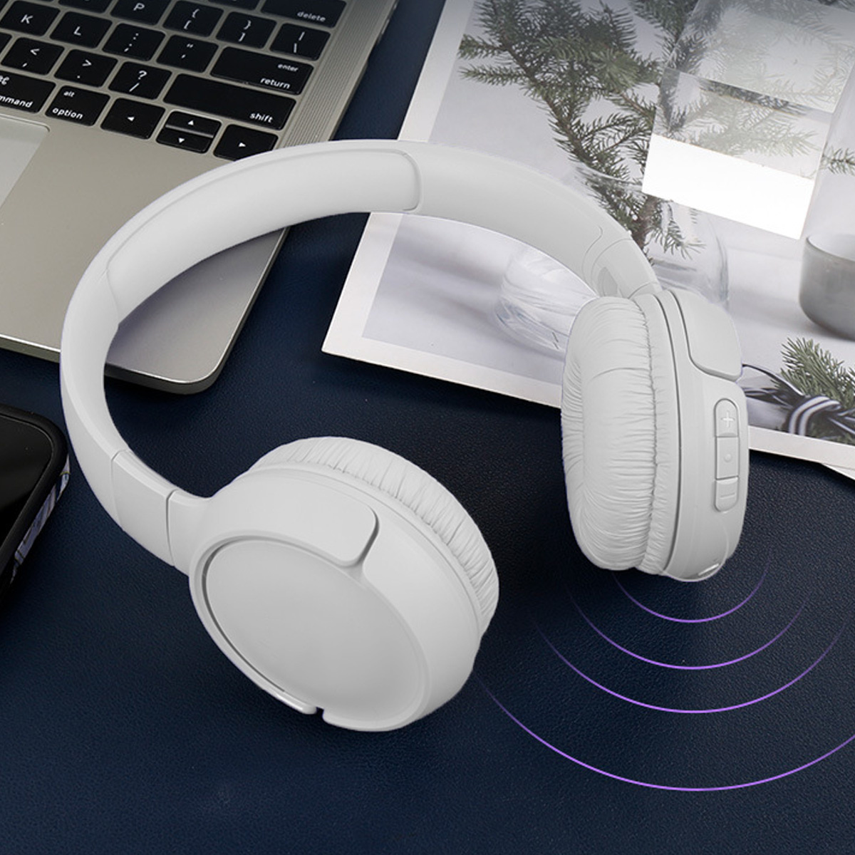 Weiße Over-Ear-Kopfhörer auf einem Schreibtisch, mit einem Laptop im Hintergrund.