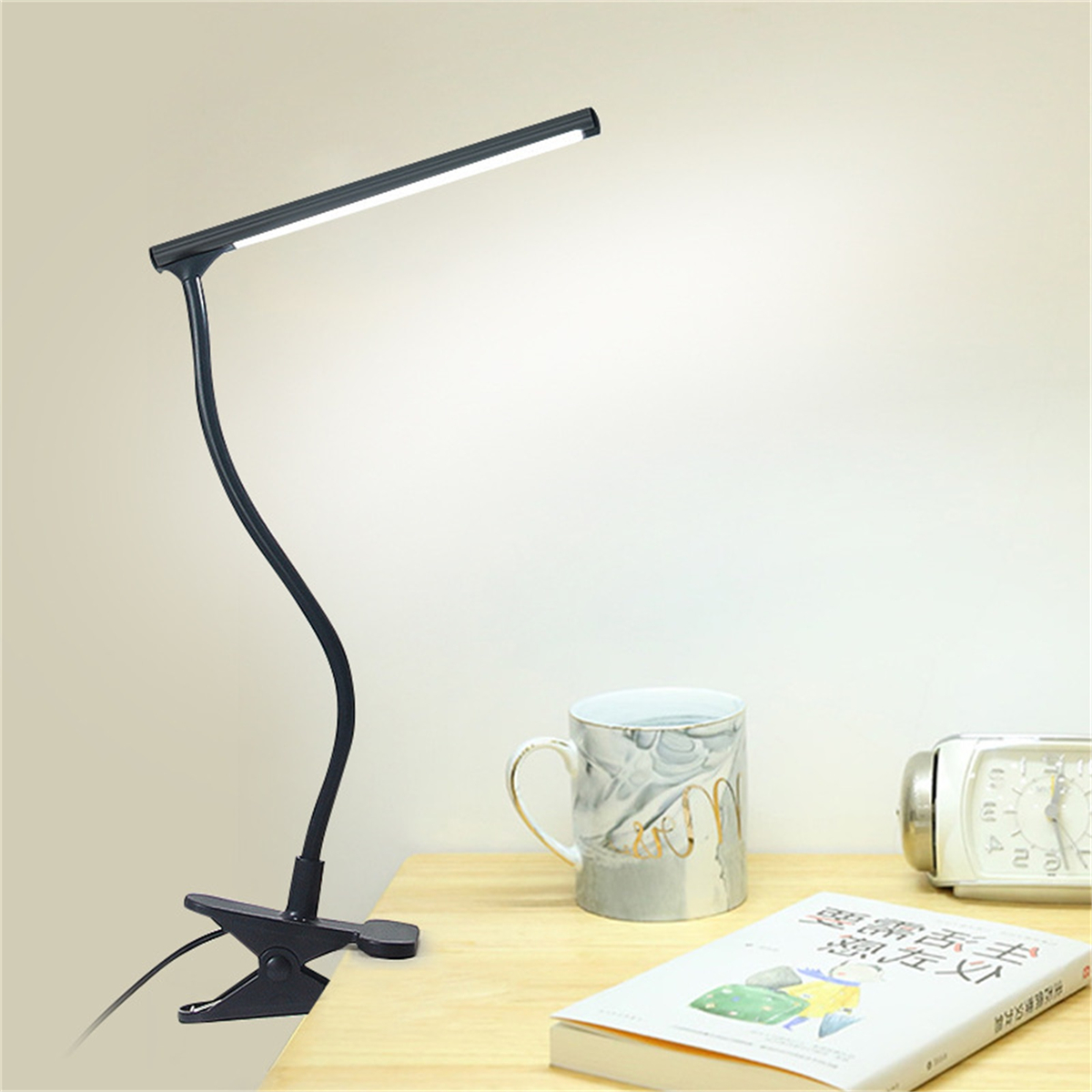 Eine schwarze Schreibtischlampe mit flexiblem Hals. Sie steht auf einem Holztisch mit einem Buch, einer Tasse und einer Uhr.