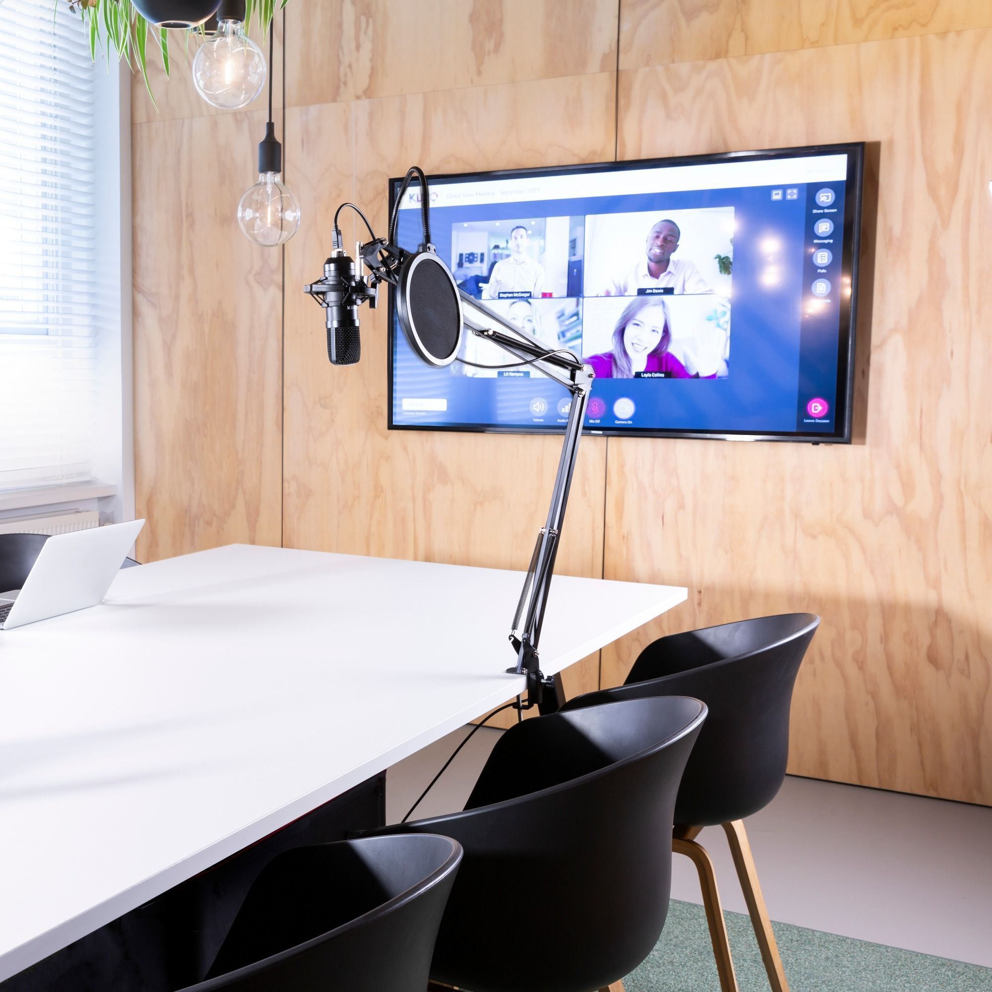 Een vergaderruimte met een groot scherm waarop een videogesprek wordt weergegeven, een microfoon en een tafel met stoelen.
