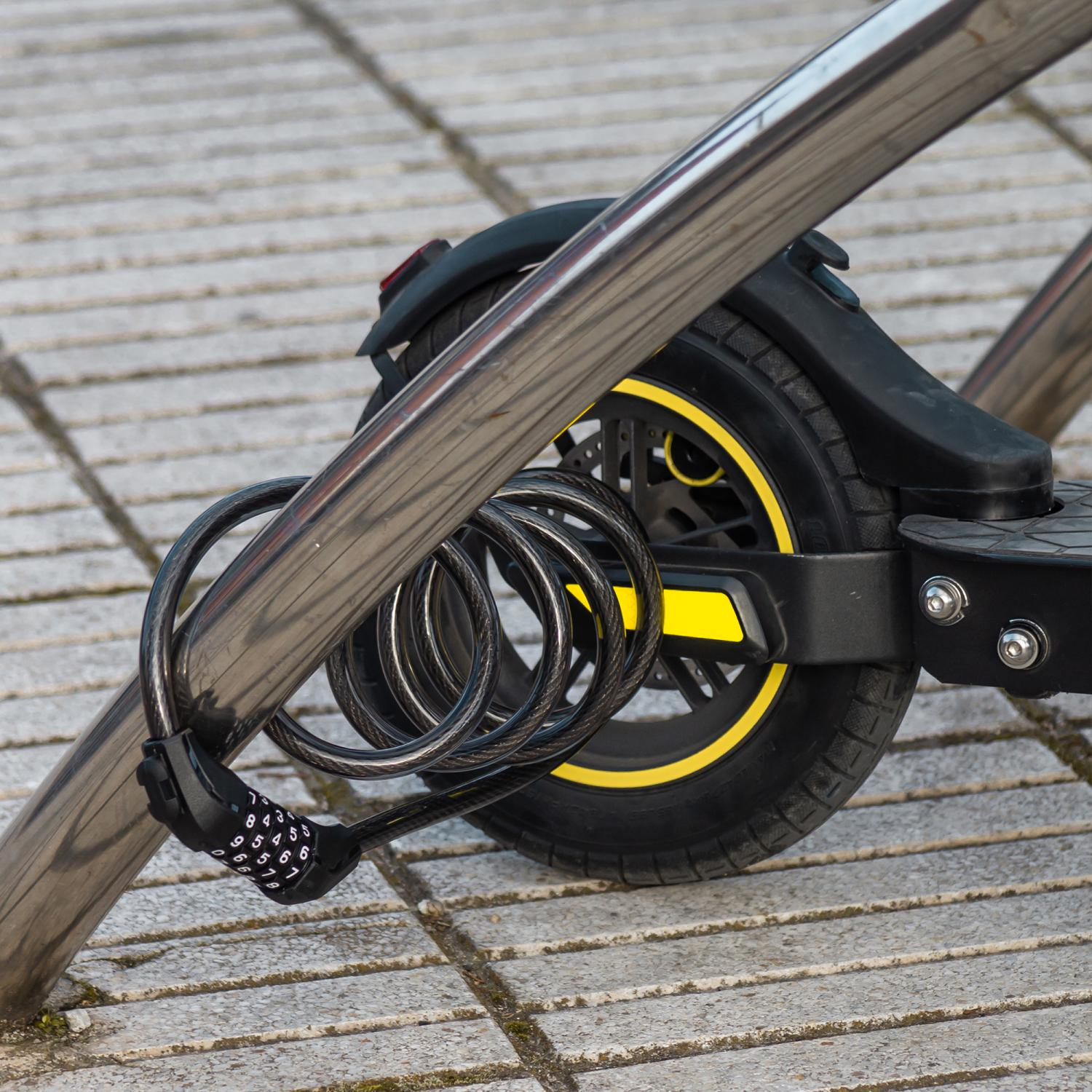 Un candado de combinación negro asegura un patinete a un poste plateado en el pavimento. El candado tiene números.
