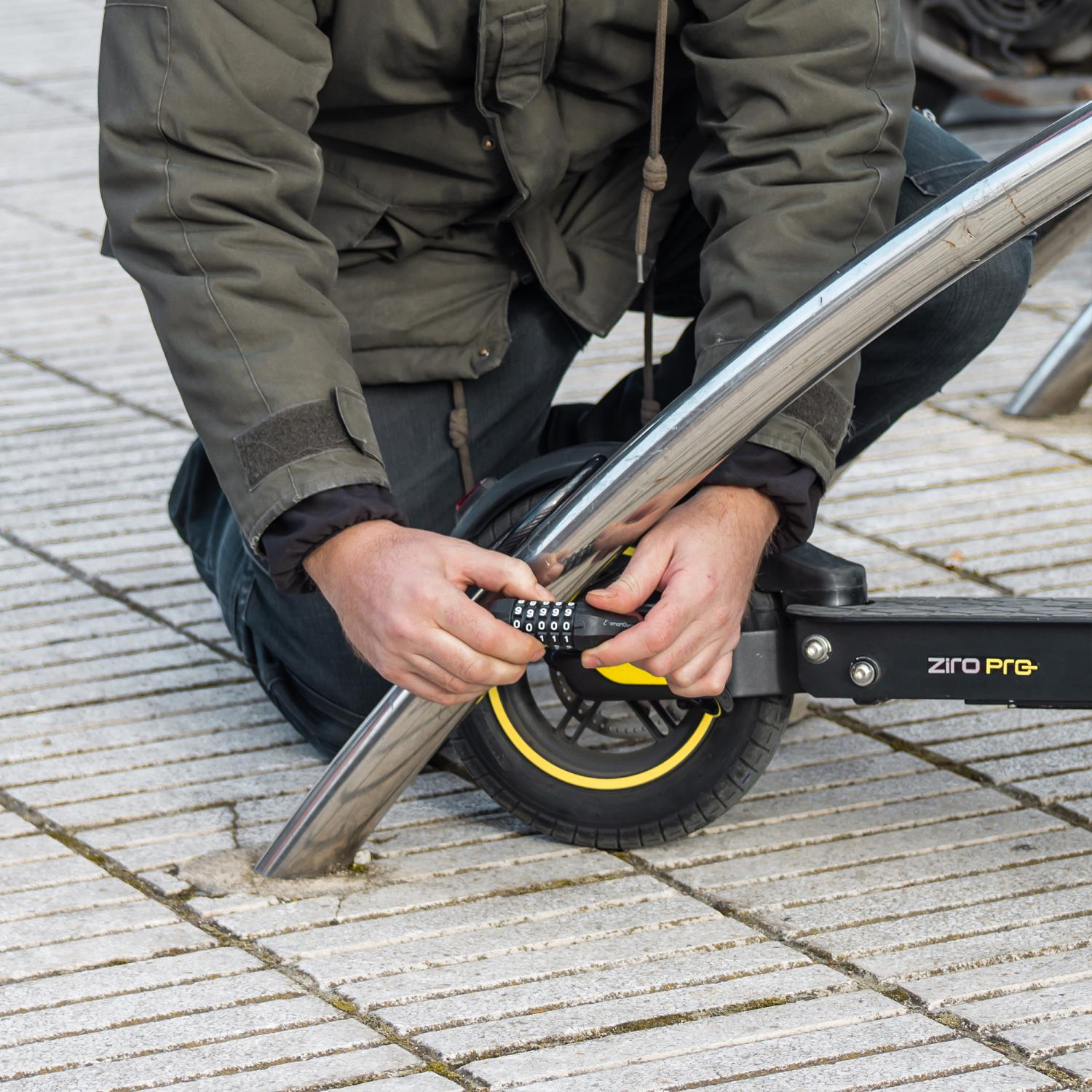 Persona usando un candado de combinación en un patinete. El patinete está en una superficie pavimentada.