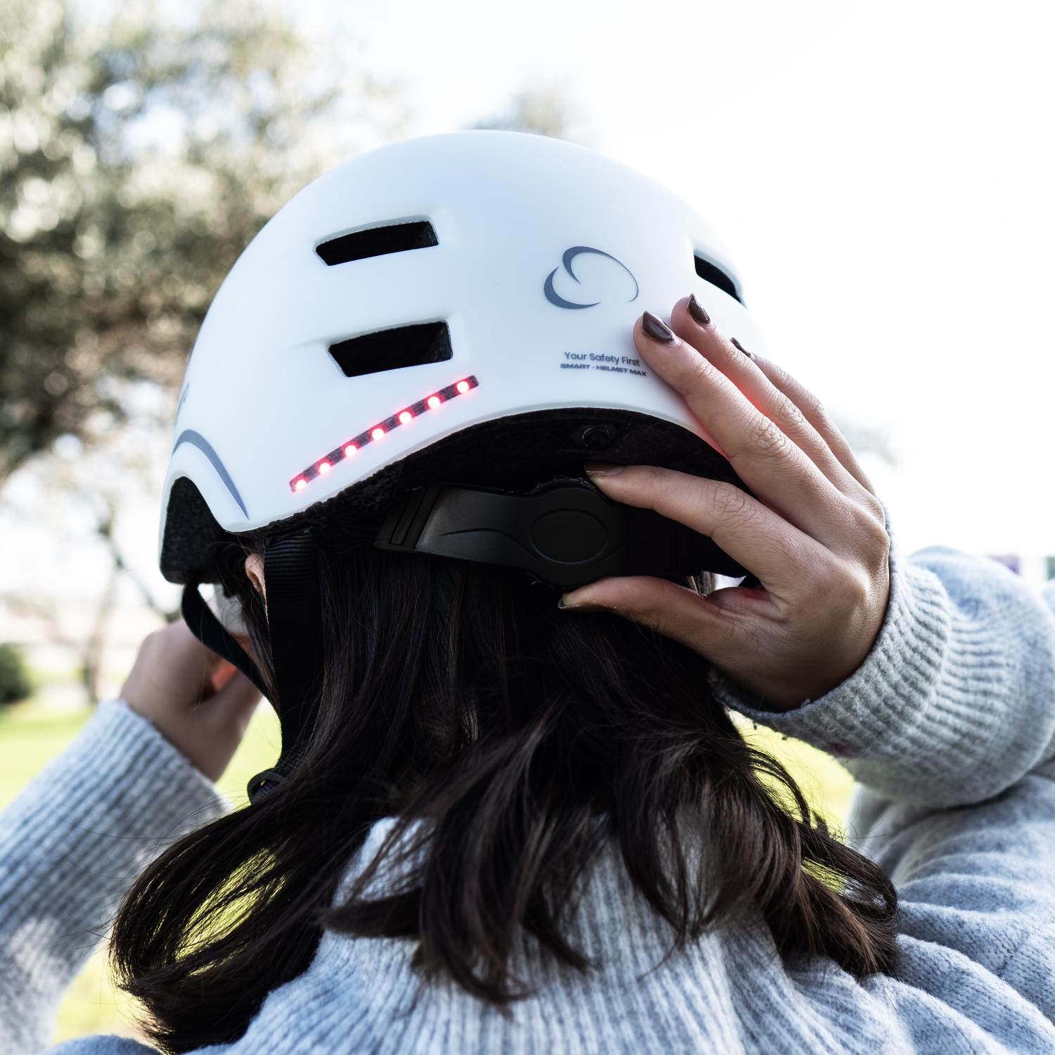 Una mujer lleva un casco de bicicleta blanco. Se ajusta la correa del casco.