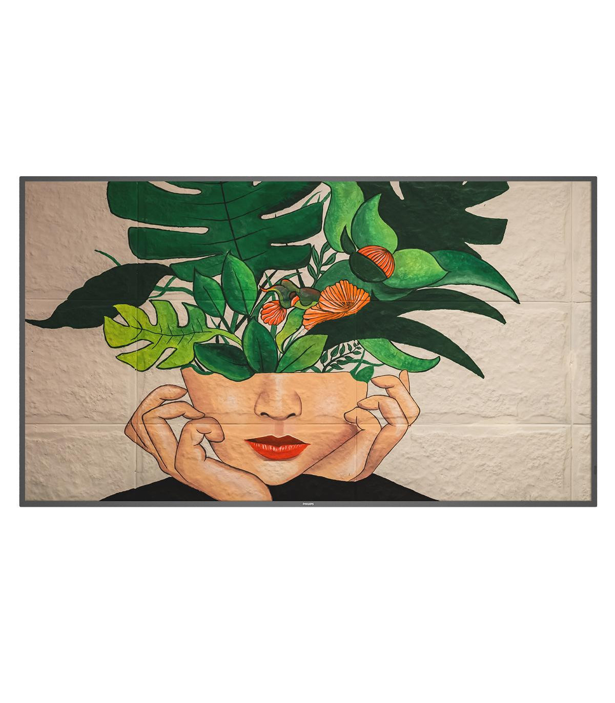Un dipinto di un volto con foglie e fiori al posto dei capelli, su un muro di mattoni chiari, visto in una cornice.