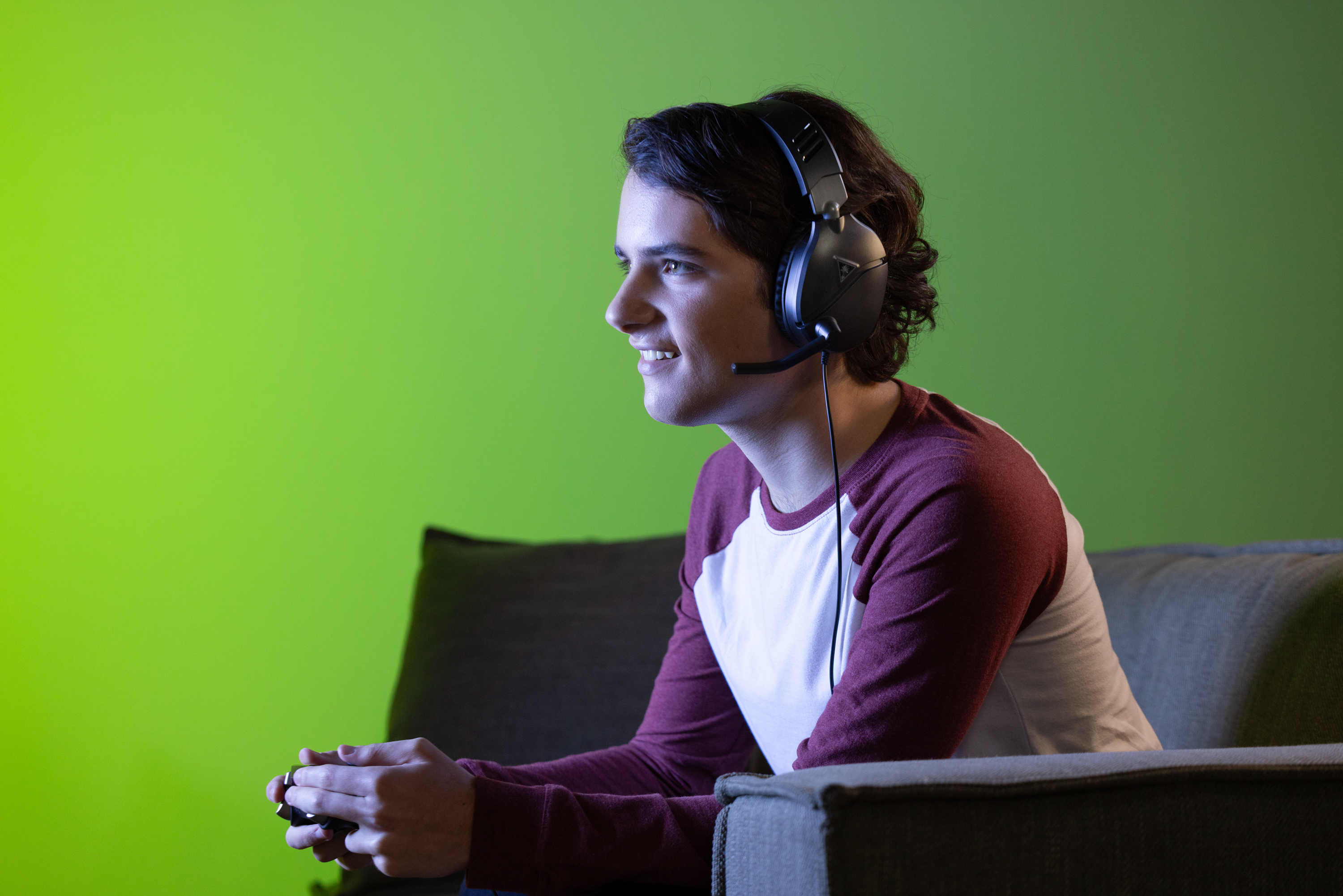 Hombre jugando con auriculares y controlador, fondo verde.