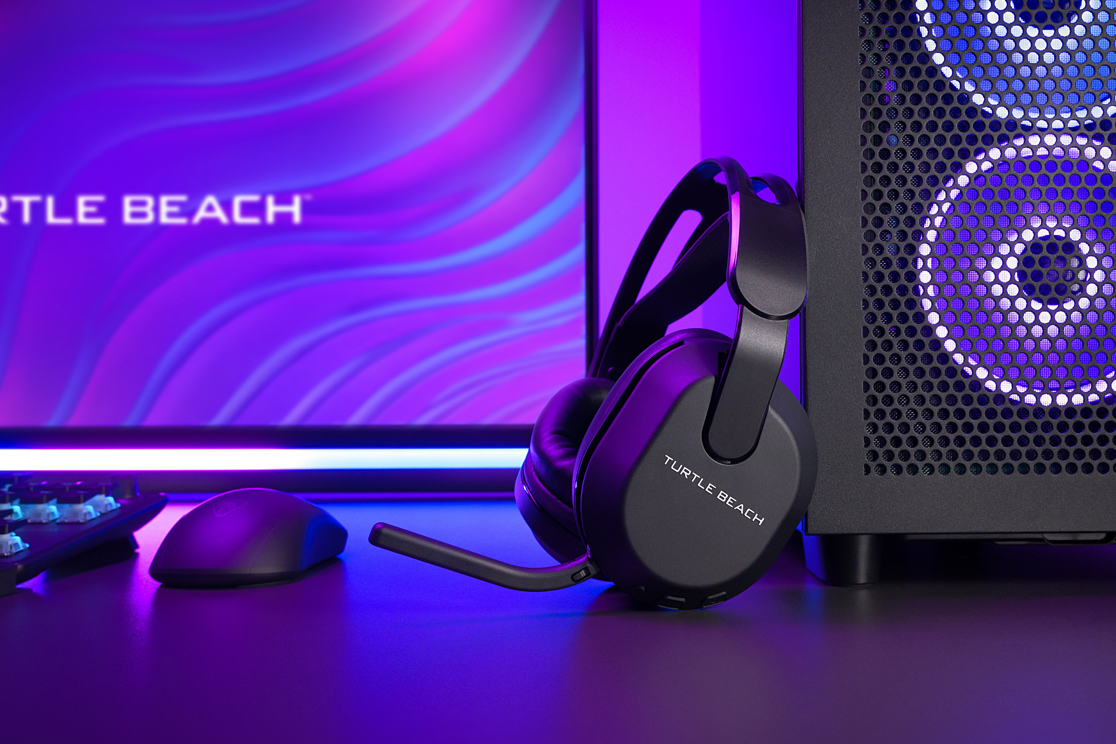 Zwarte Turtle Beach headset en muis op een bureau, computermonitor op de achtergrond.