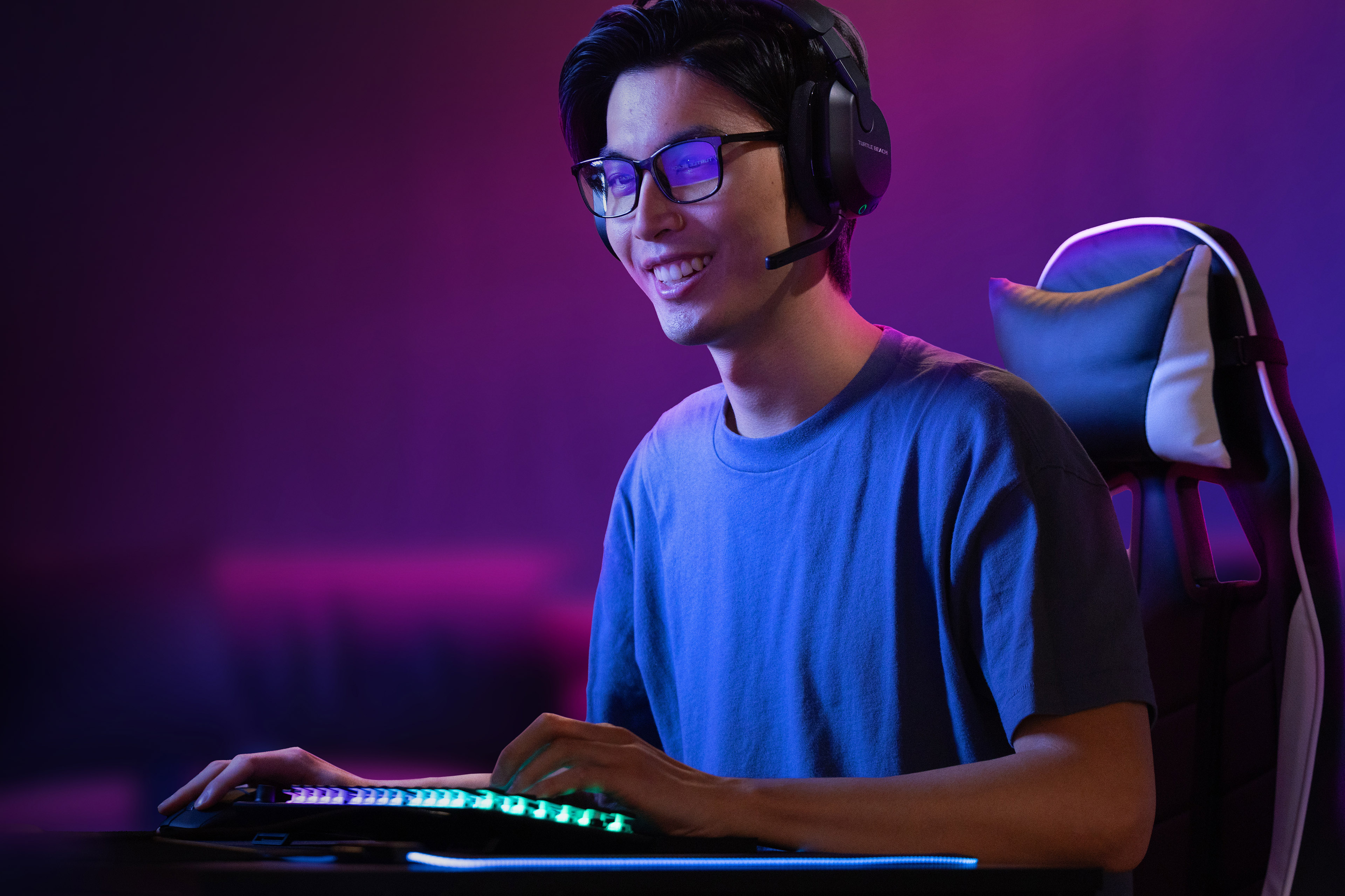 Mężczyzna w okularach gra, ma na sobie zestaw słuchawkowy i używa klawiatury z zielonymi światłami.