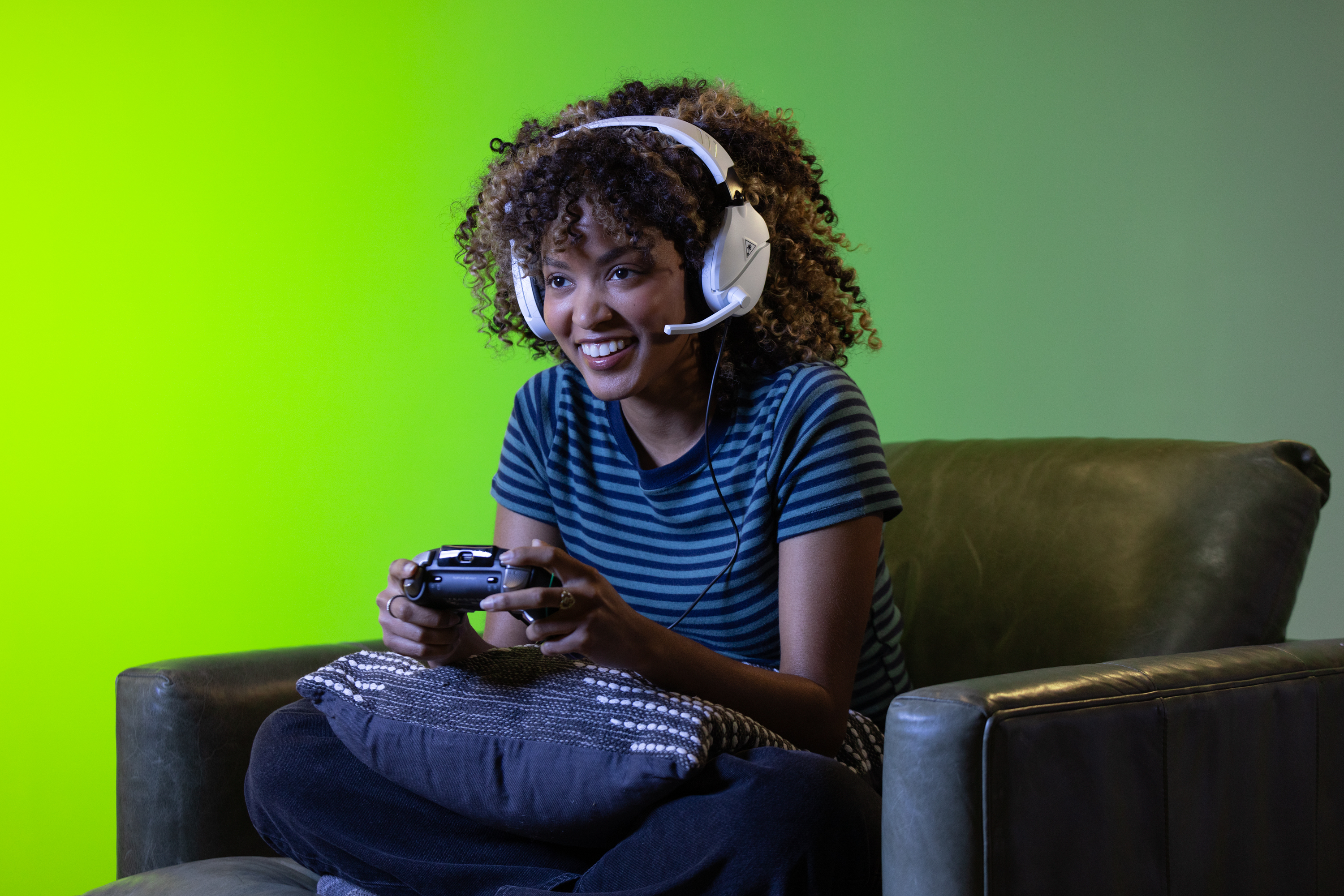 Eine Frau mit Headset spielt ein Videospiel. Sie lächelt und hält einen Controller.