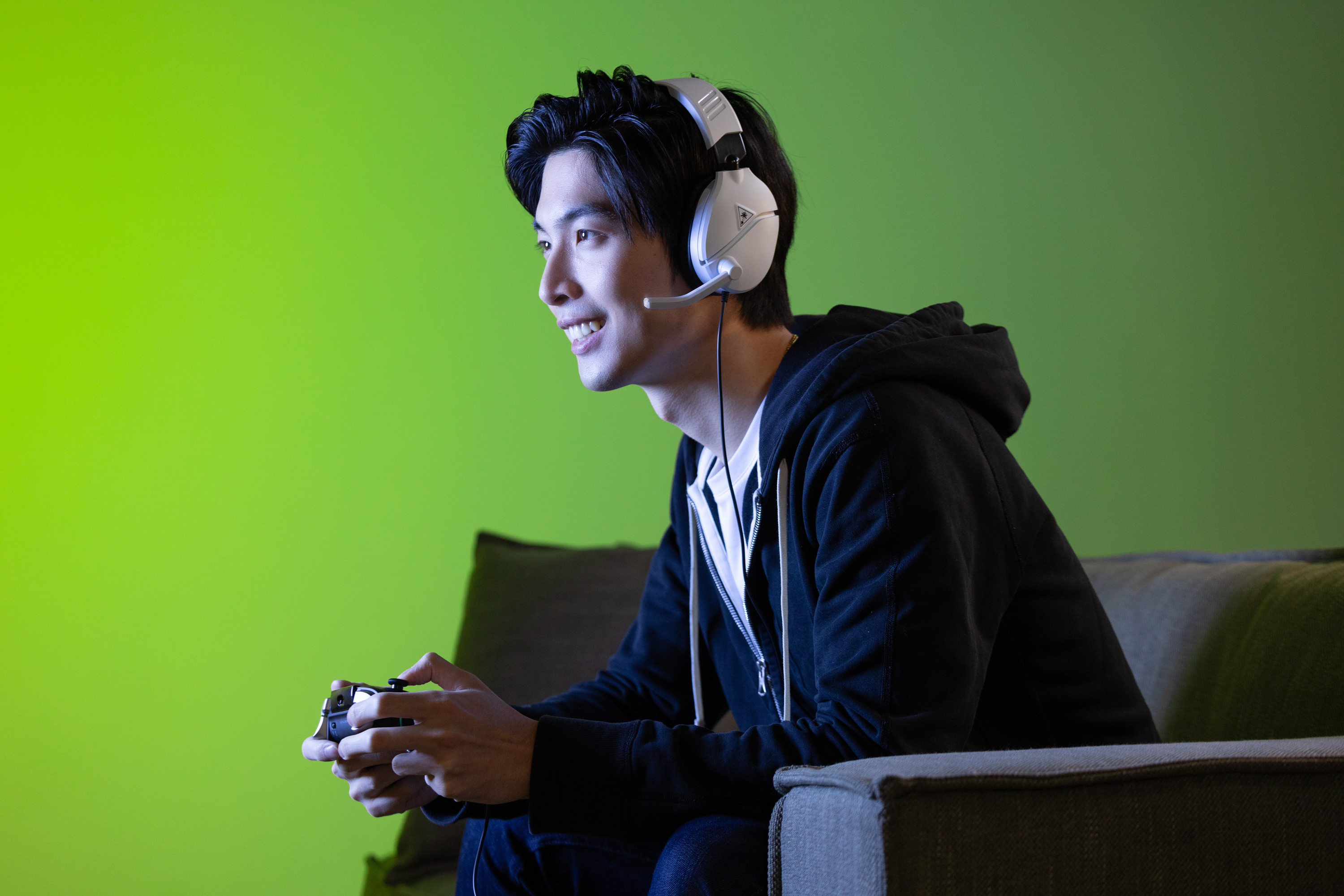 Ein Mann mit Headset spielt Videospiele auf einem Sofa. Grüner Hintergrund.