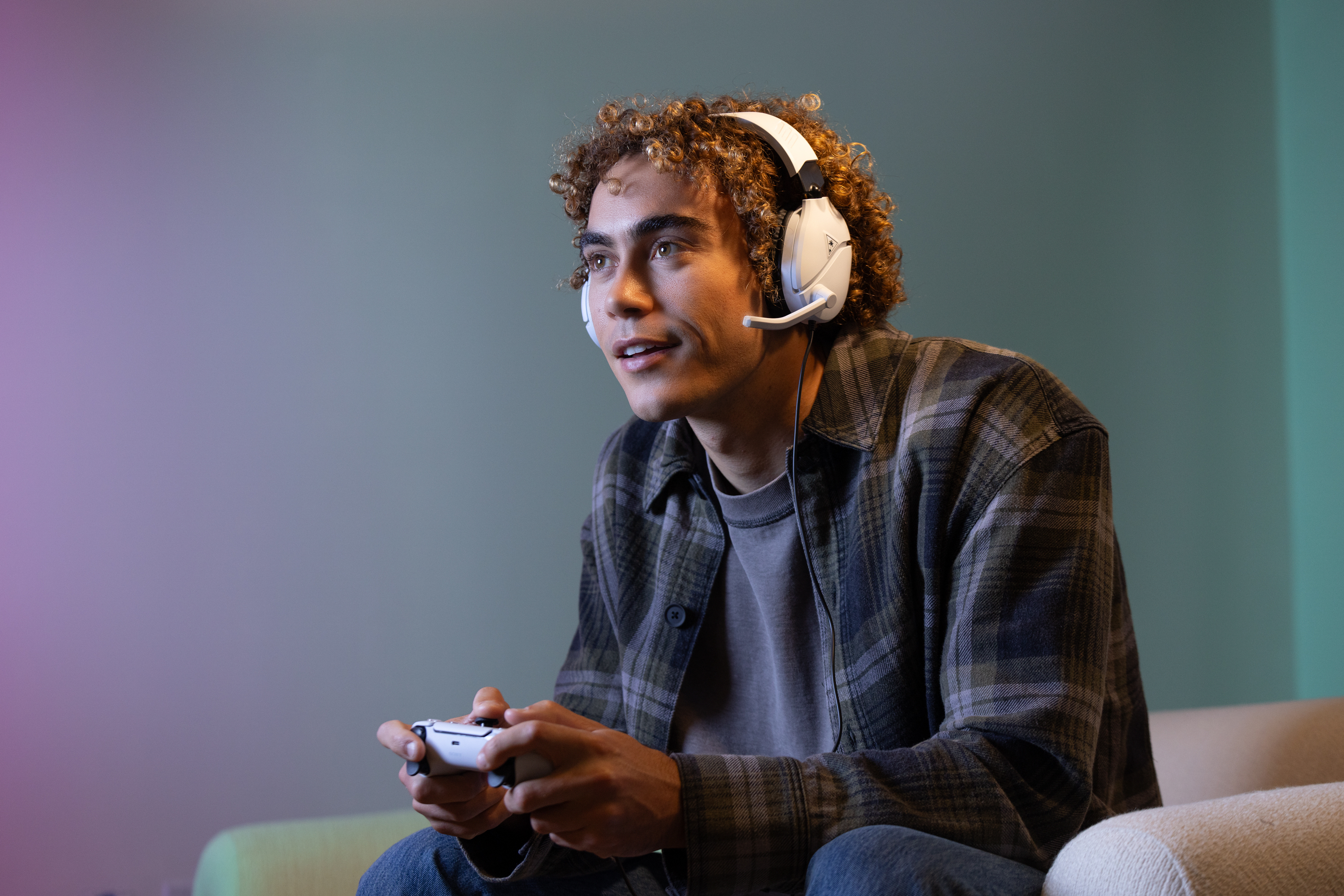 A young man wearing headphones, holding a controller, looking at the screen.
