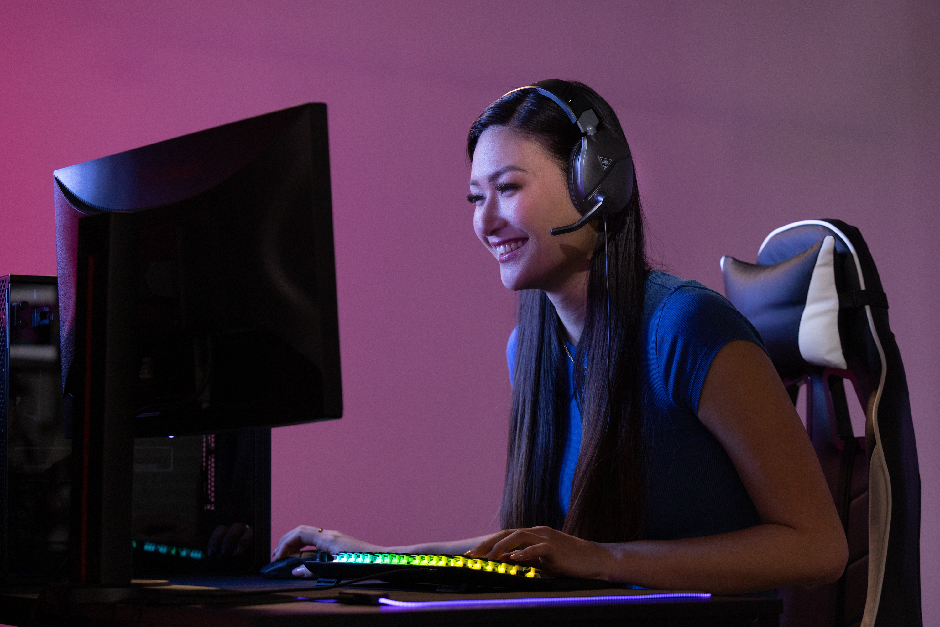 Kobieta gra na komputerze w słuchawkach, uśmiechnięta.