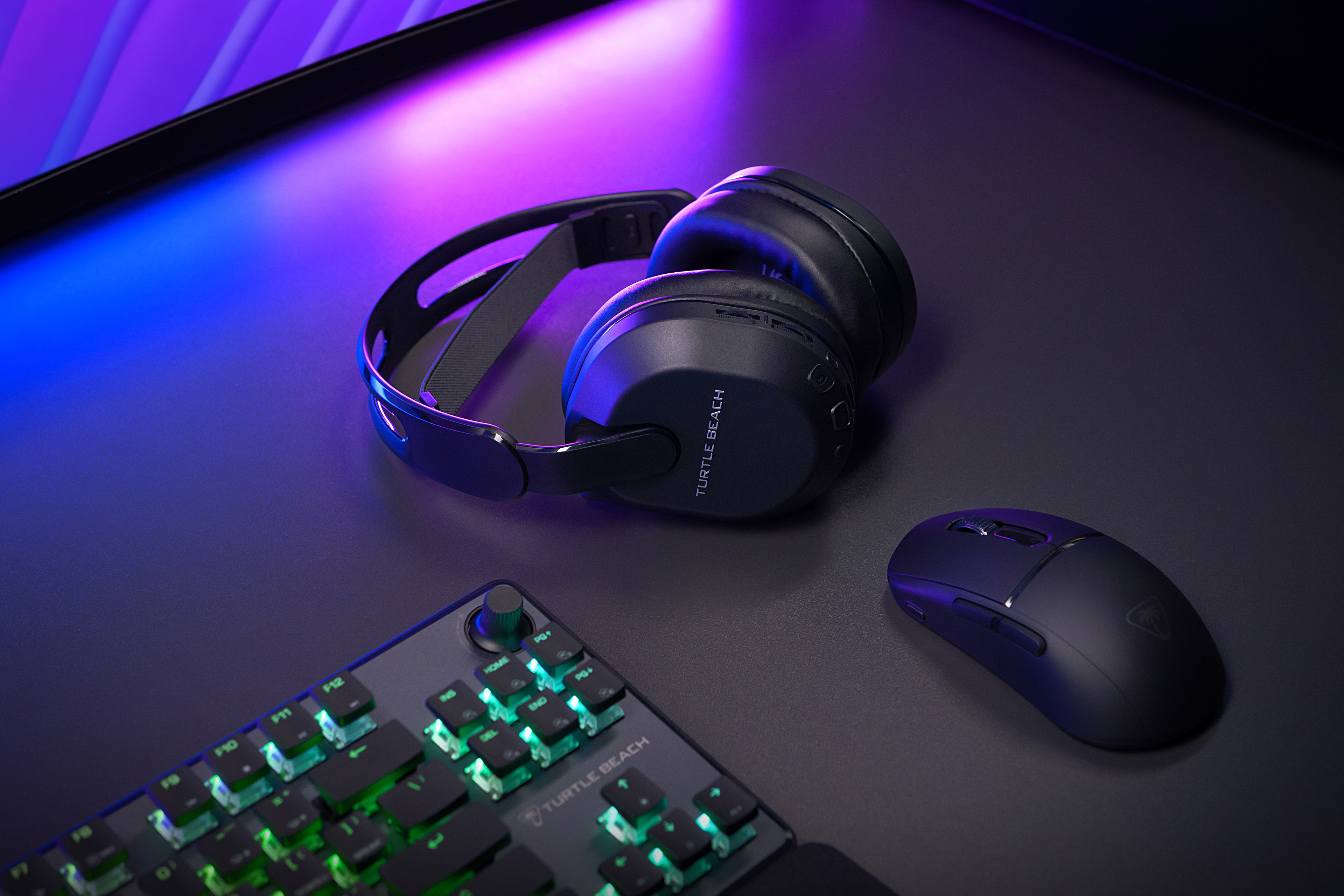 Czarny zestaw słuchawkowy Turtle Beach, klawiatura i mysz na biurku. Biurko jest czarne z niebieskimi i fioletowymi światłami.