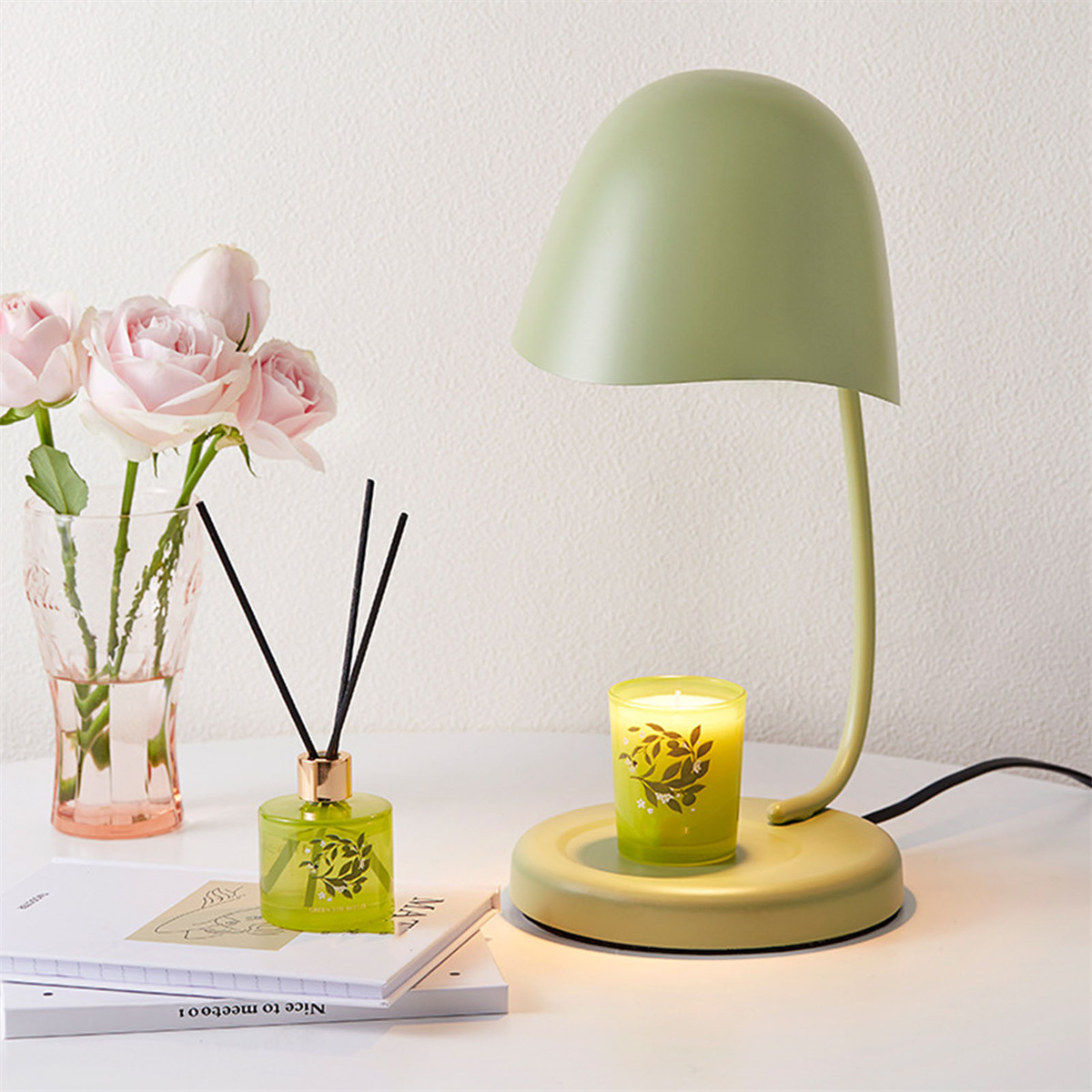 Eine Lampe, eine Kerze und ein Diffusor auf einem Tisch. Ein Rosenstrauß befindet sich links.