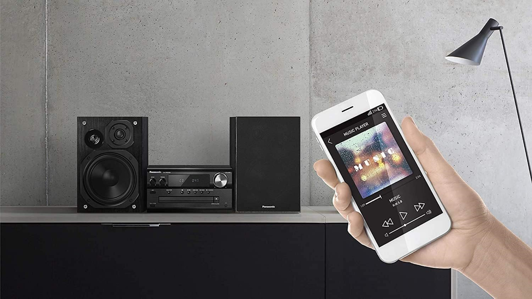 Una mano tiene un telefono con app per lettore musicale vicino a altoparlanti e stereo.