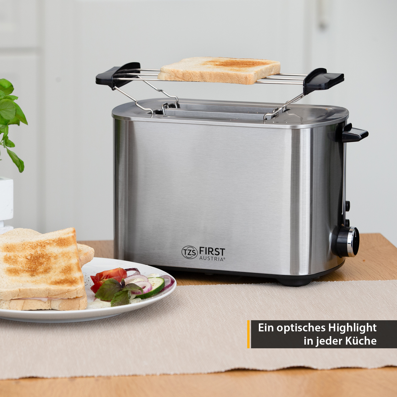 Ein silberner Toaster mit zwei Scheiben Toastbrot, ein Teller mit Essen auf einem Tisch.