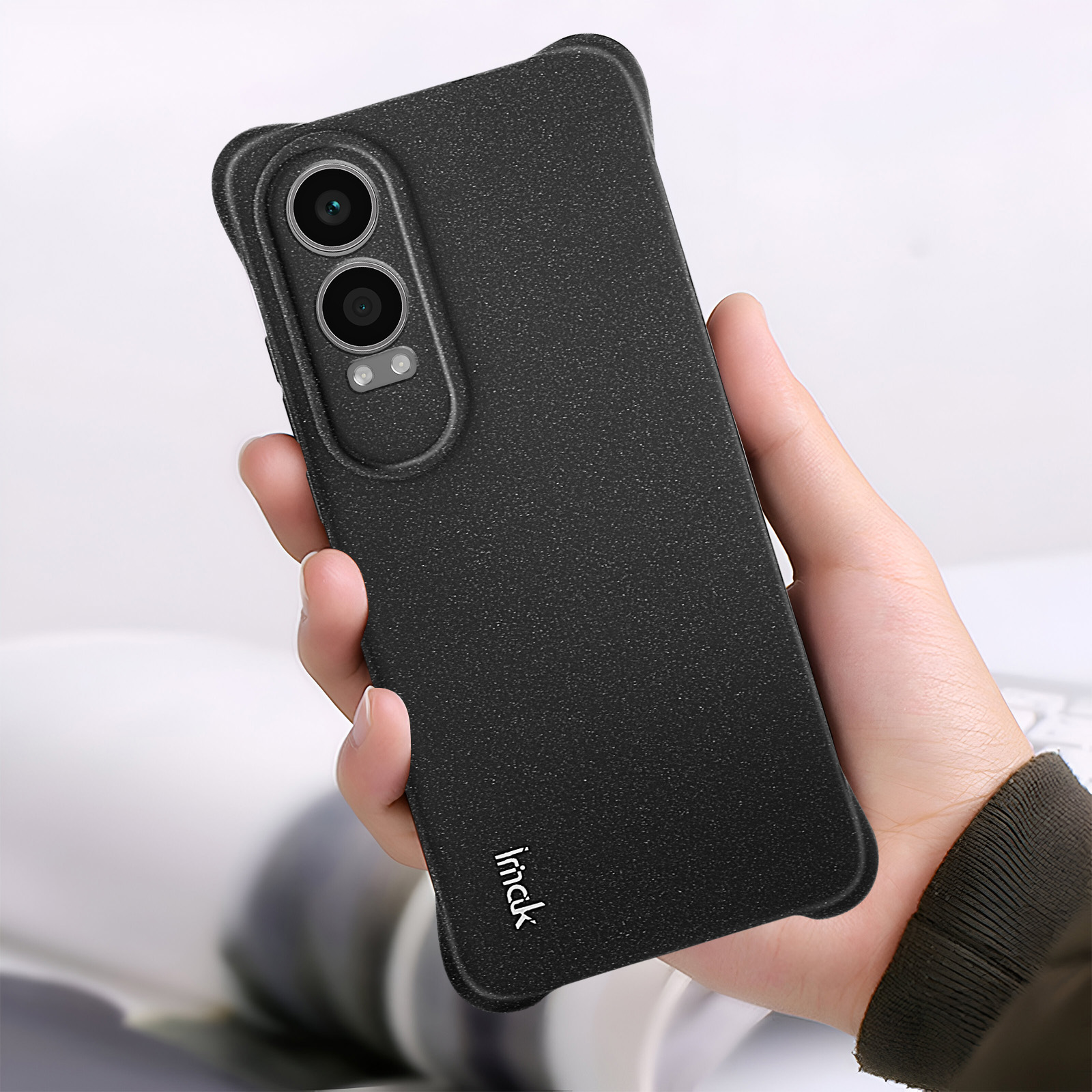 Una mano che tiene una custodia nera per telefono. La custodia ha due fori per la fotocamera e una superficie strutturata.