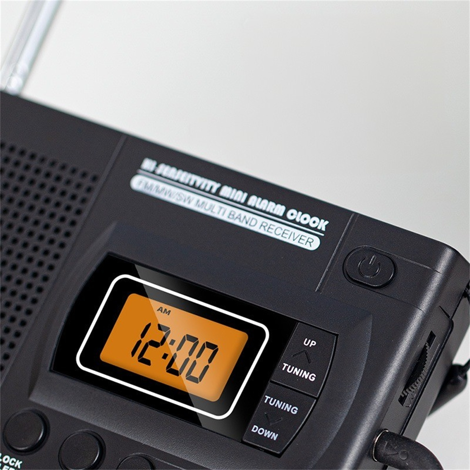 Ein schwarzer Mini-Wecker mit einer orangefarbenen Digitalanzeige, die 12:00 Uhr anzeigt. Tasten mit der Aufschrift 'Tuning' und 'Up/Down' sind sichtbar.