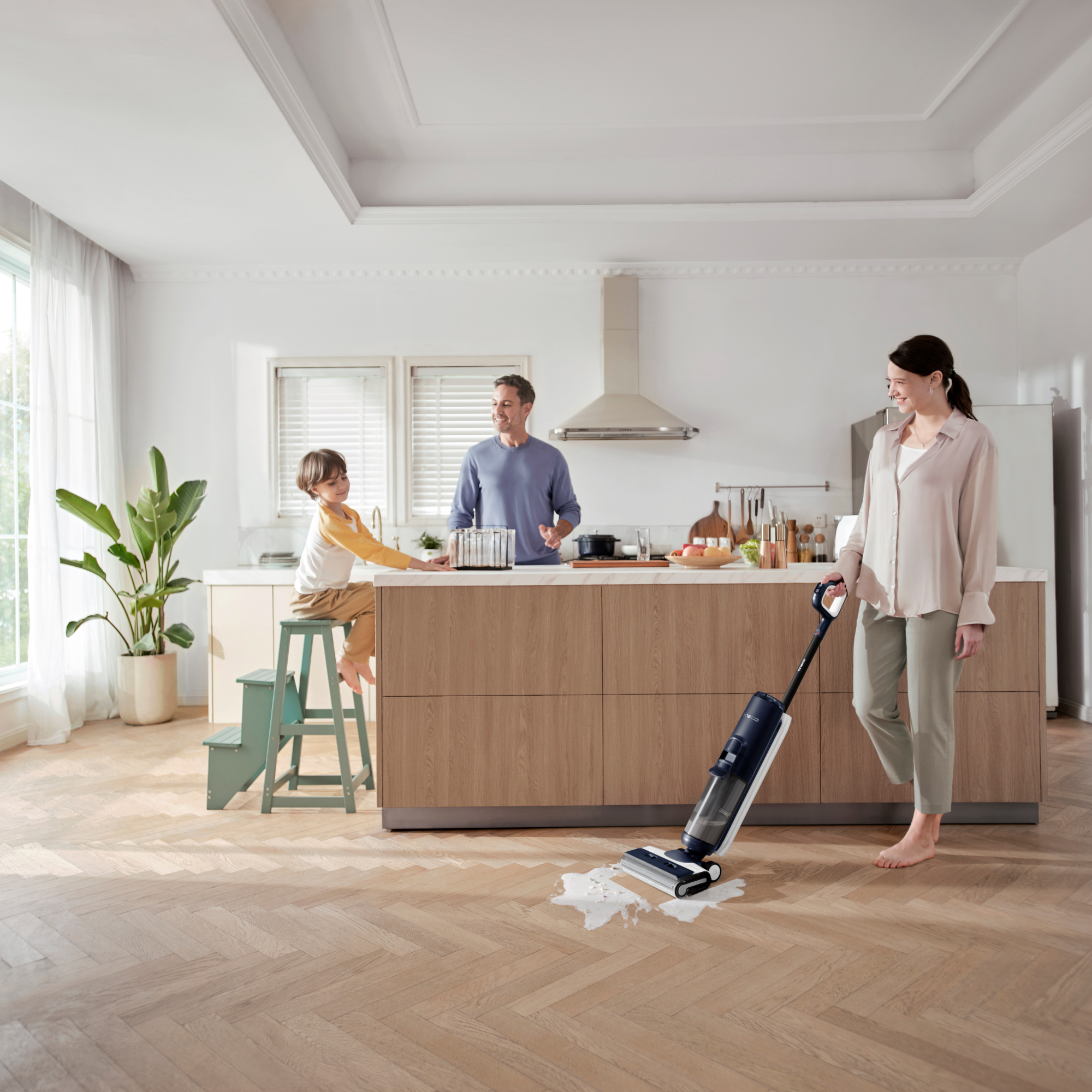 Rodzina w kuchni używająca myjki do podłóg. Chłopiec siedzi na stołku.