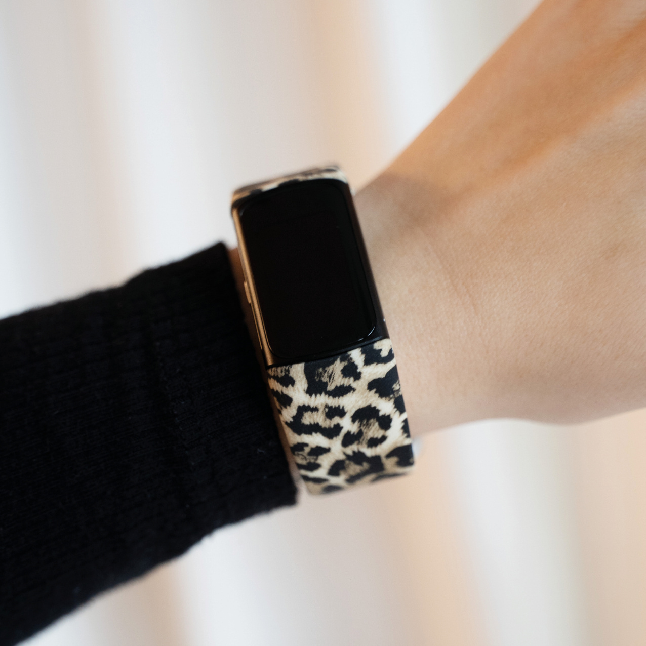 Handgelenk mit Leopardenmuster-Armband an einer schwarzen Smartwatch.