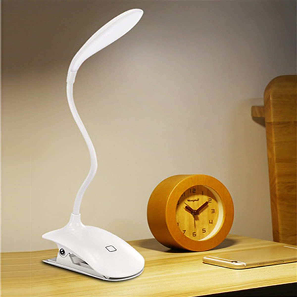 Weiße Schreibtischlampe mit flexiblem Hals und eine Holzuhr auf einem Holzschreibtisch.