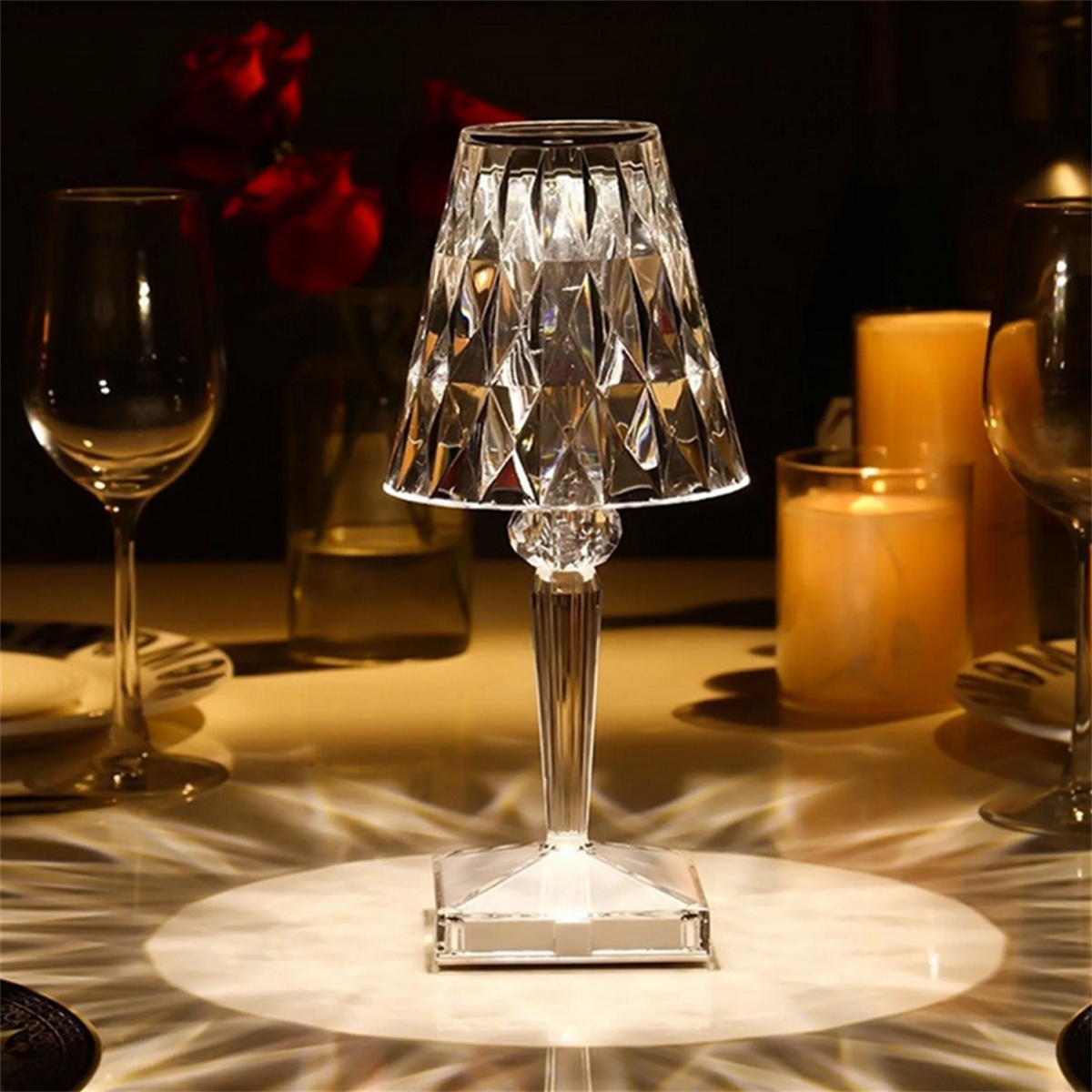 Kristall-Tischlampe mit facettiertem Schirm, wirft Licht auf Tisch mit Kerzen und Gläsern.