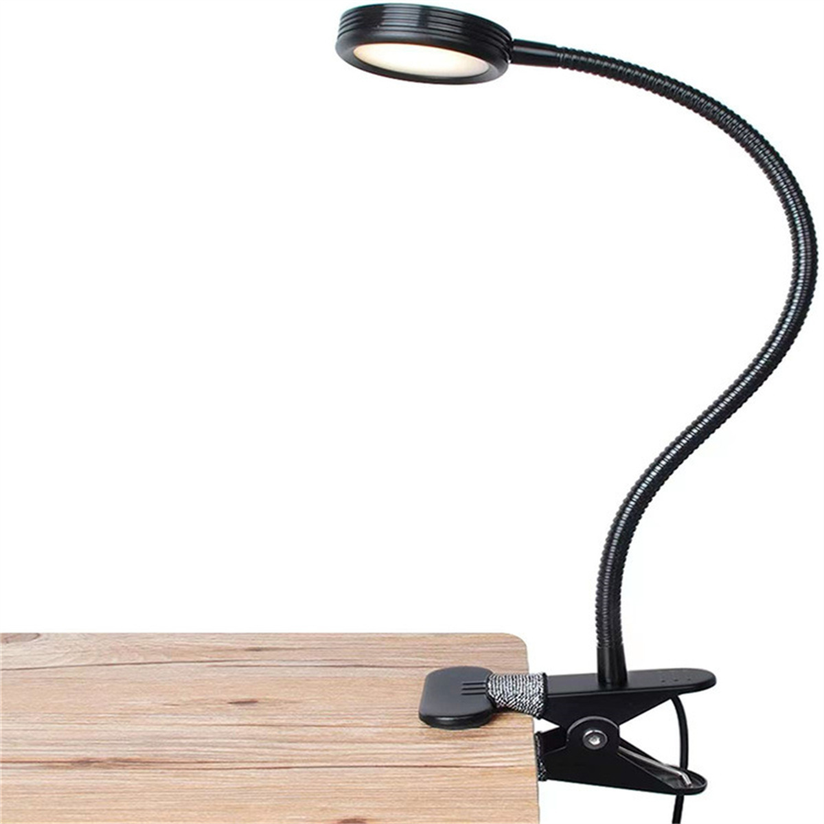 Eine schwarze Schreibtischlampe mit flexiblem Hals und Klemmfuß, auf einem Holzschreibtisch. Die Lampe ist eingeschaltet.