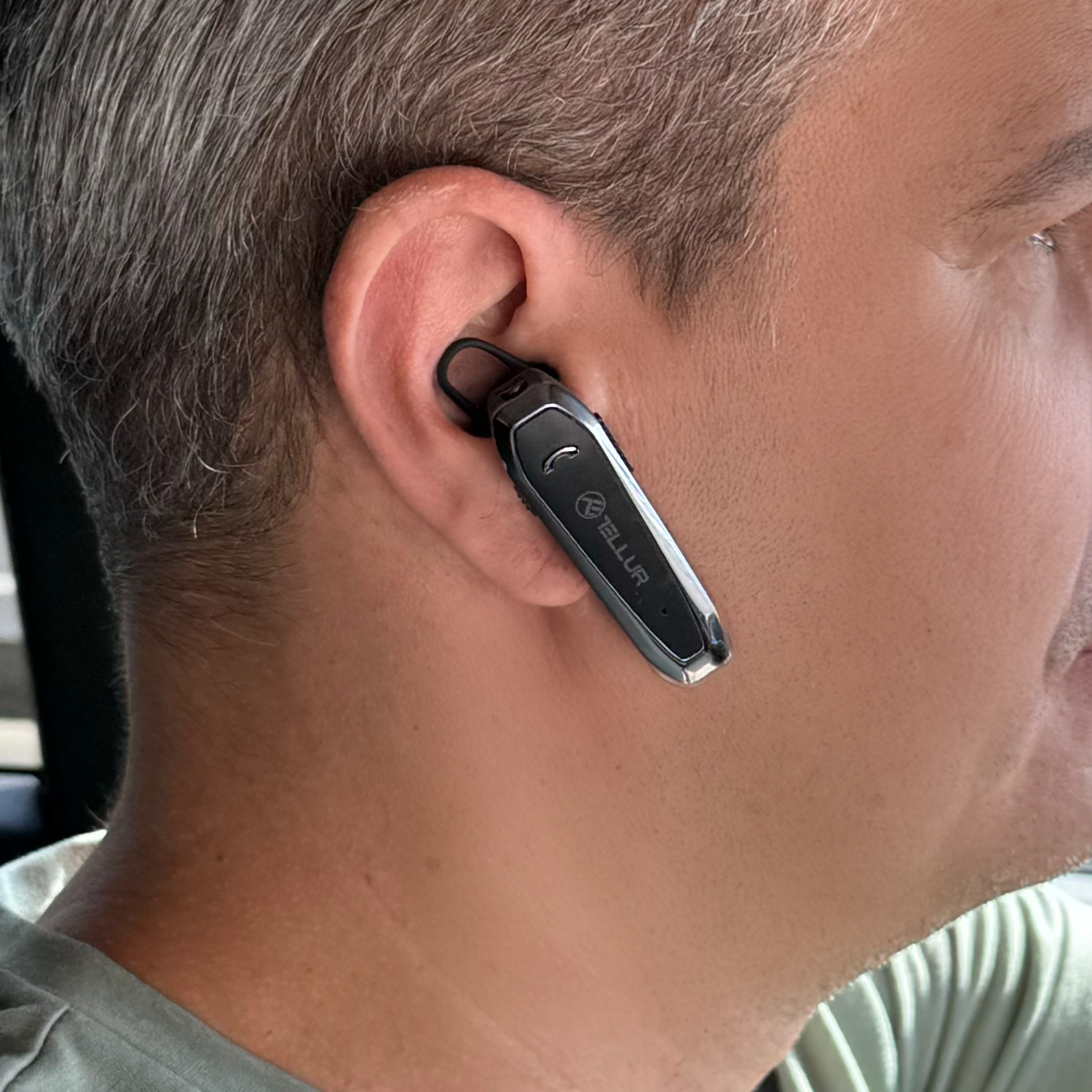 Person trägt ein schwarzes, schlankes Bluetooth-Headset im Ohr.