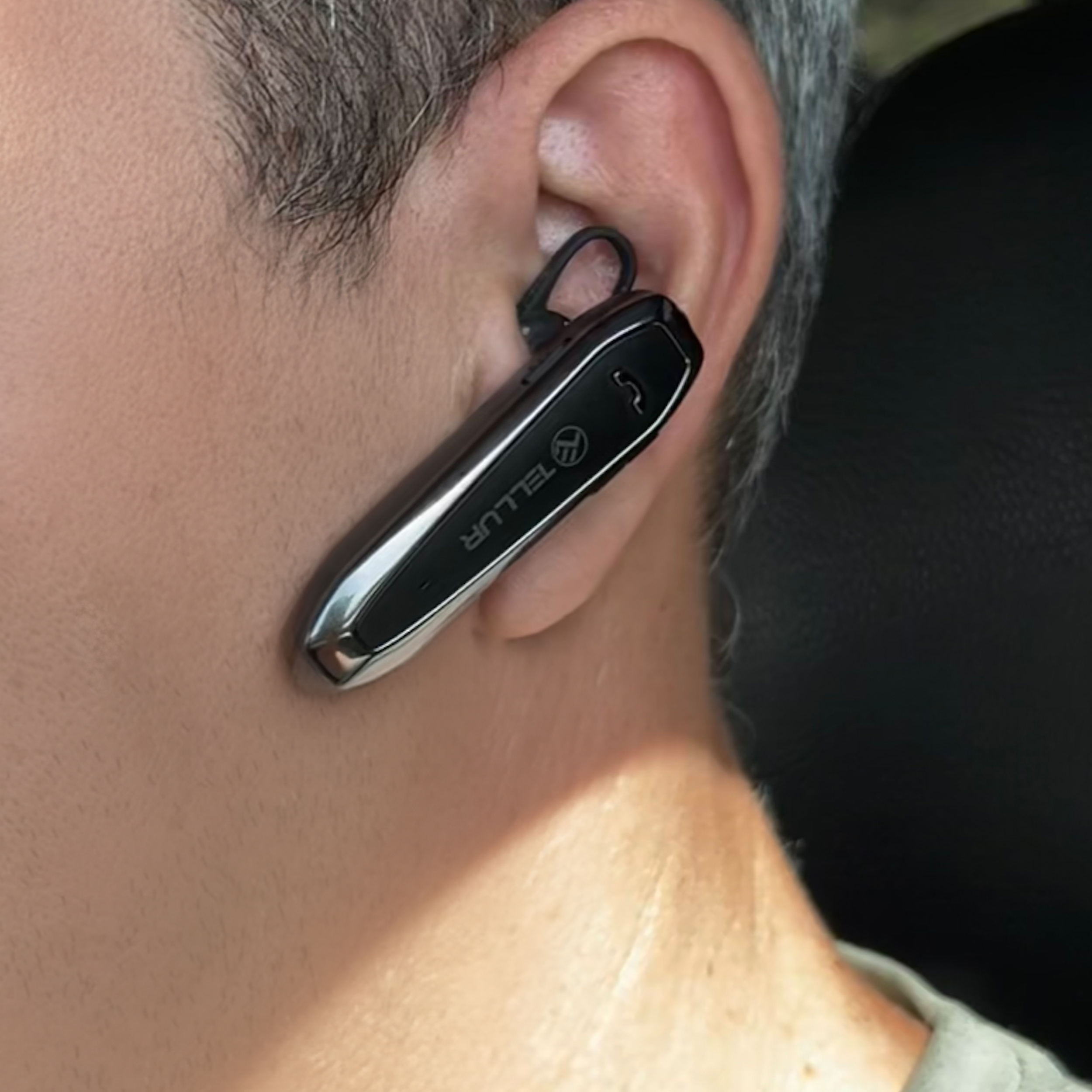 Ein Mann, der ein schwarzes Bluetooth-Headset im Ohr trägt. Das Headset ist silber und schwarz.