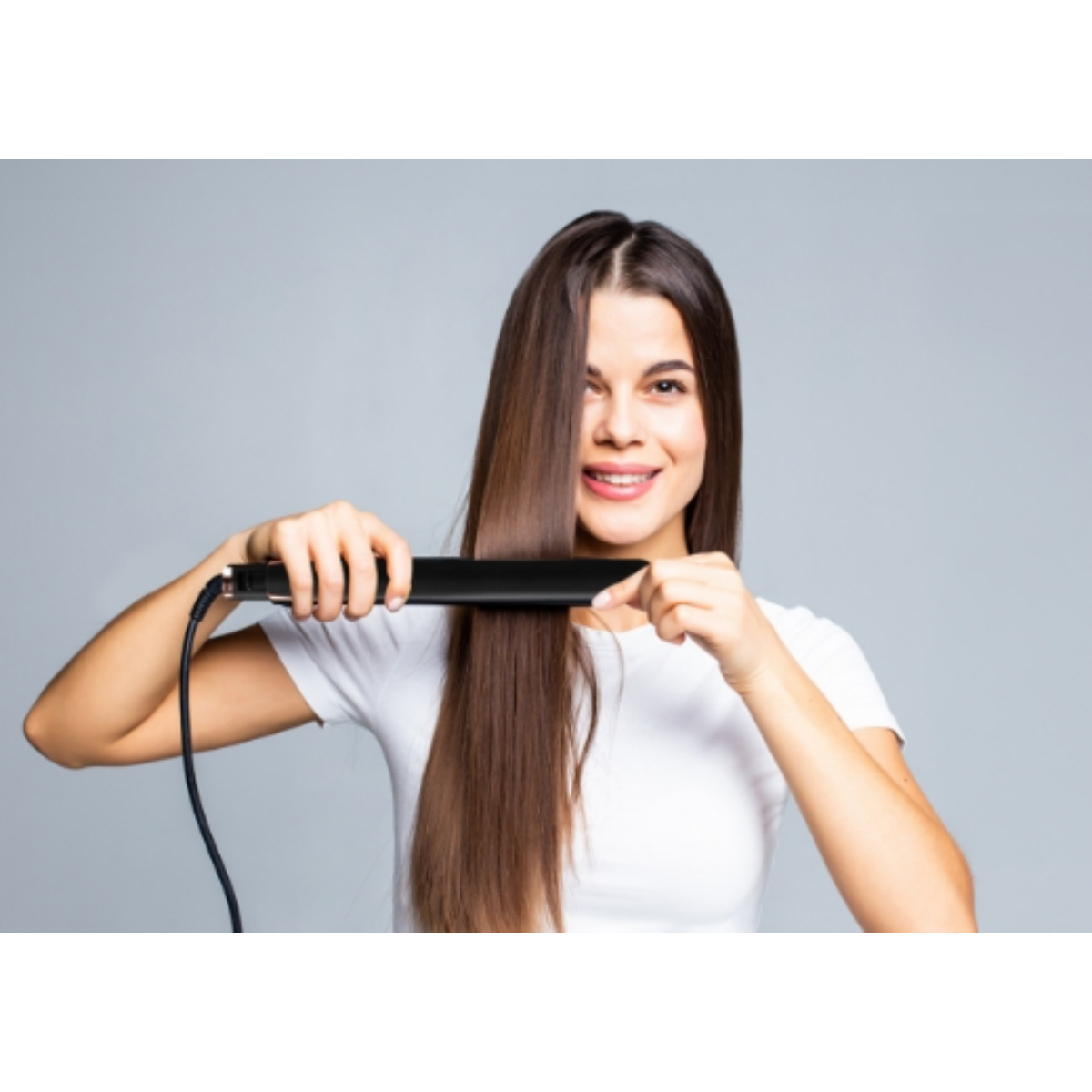 Una donna con lunghi capelli castani usa una piastra nera, sorridendo.