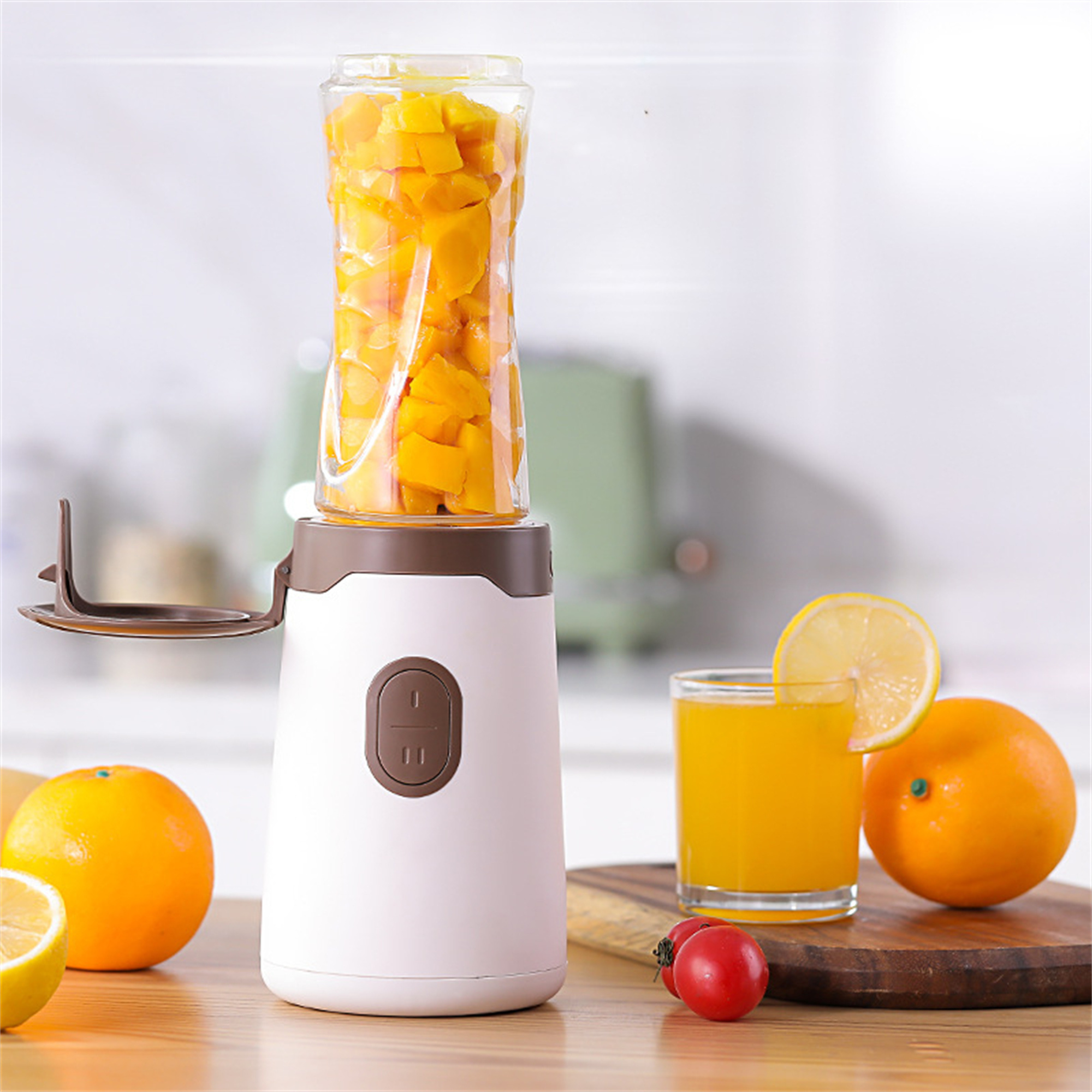 Ein Mixer mit gelben Mangos, ein Glas Saft mit Zitronenscheibe und Orangen auf einem Holzbrett.