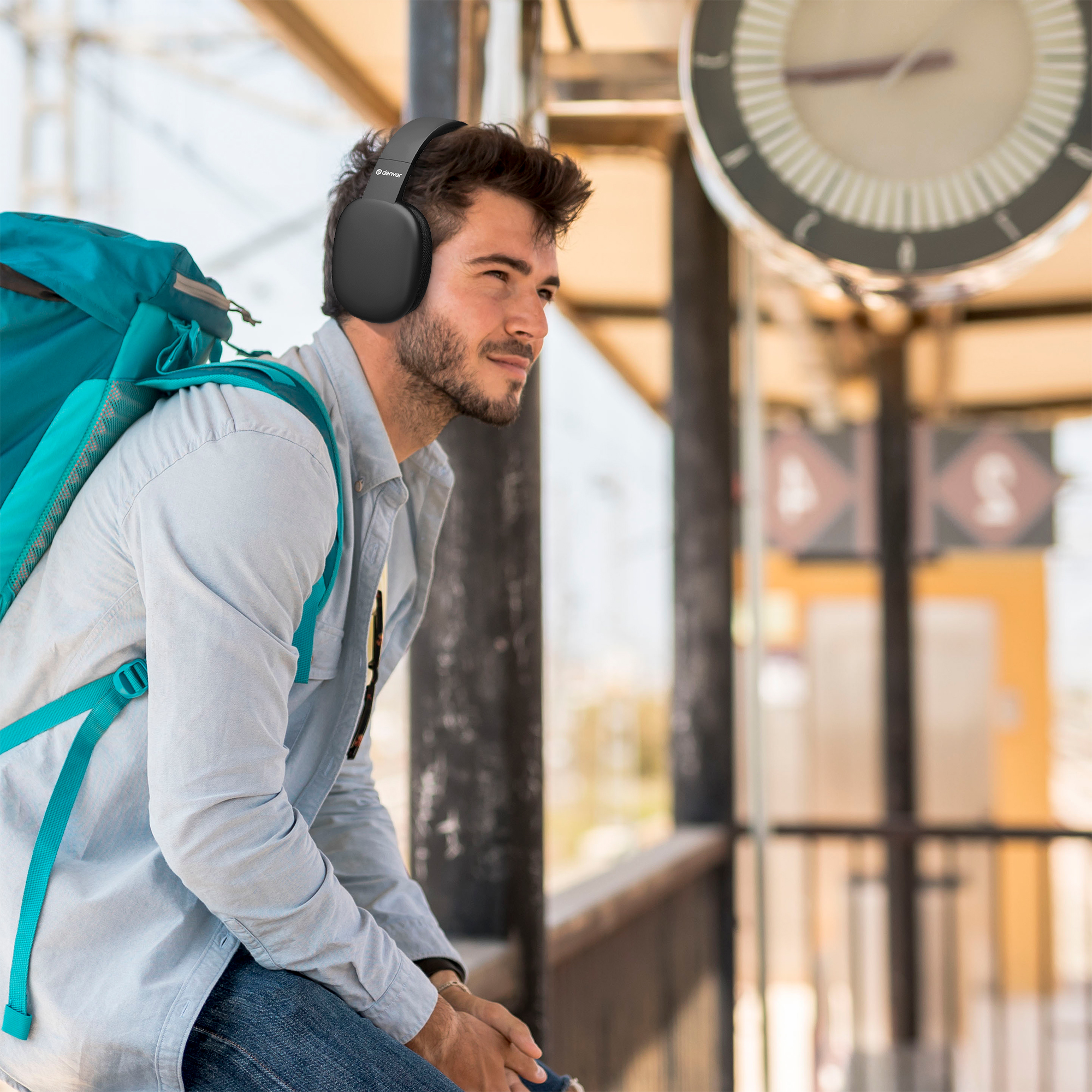 Mężczyzna w słuchawkach na dworcu, patrzący w bok.