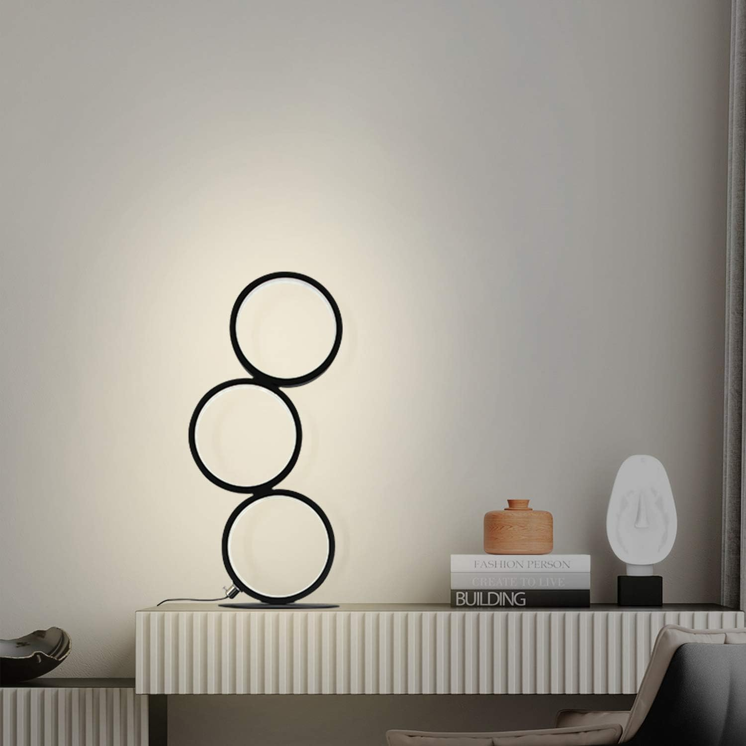 Nowoczesna czarna lampa z trzema okrągłymi światłami, na białej komodzie, na tle białej ściany.