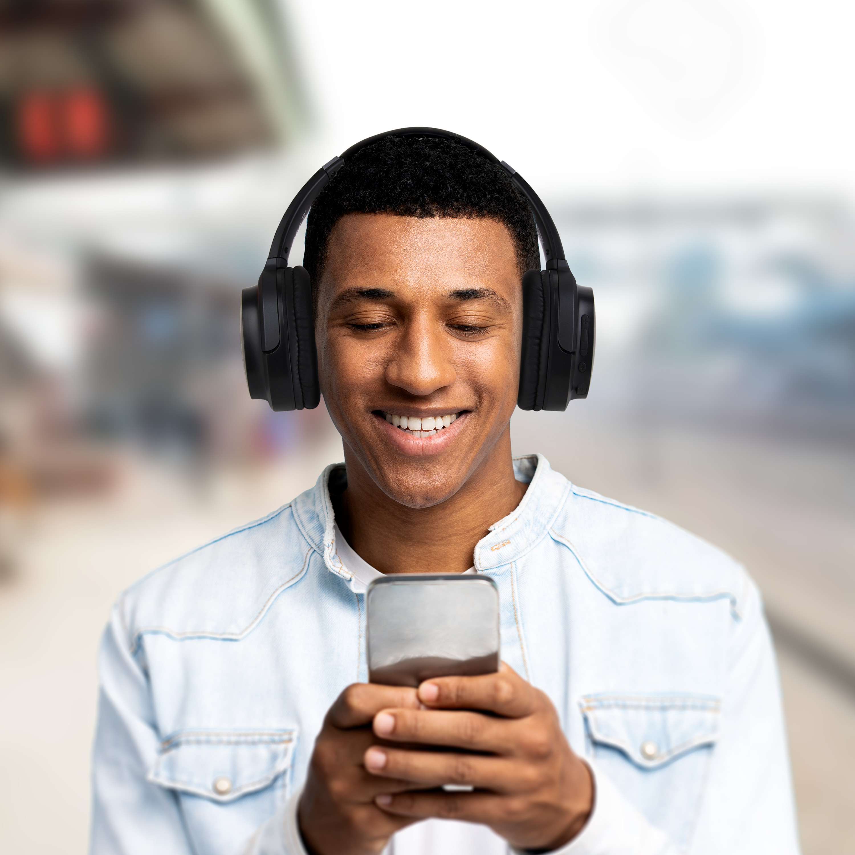 Uśmiechnięty mężczyzna w czarnych słuchawkach, patrzący na smartfon.