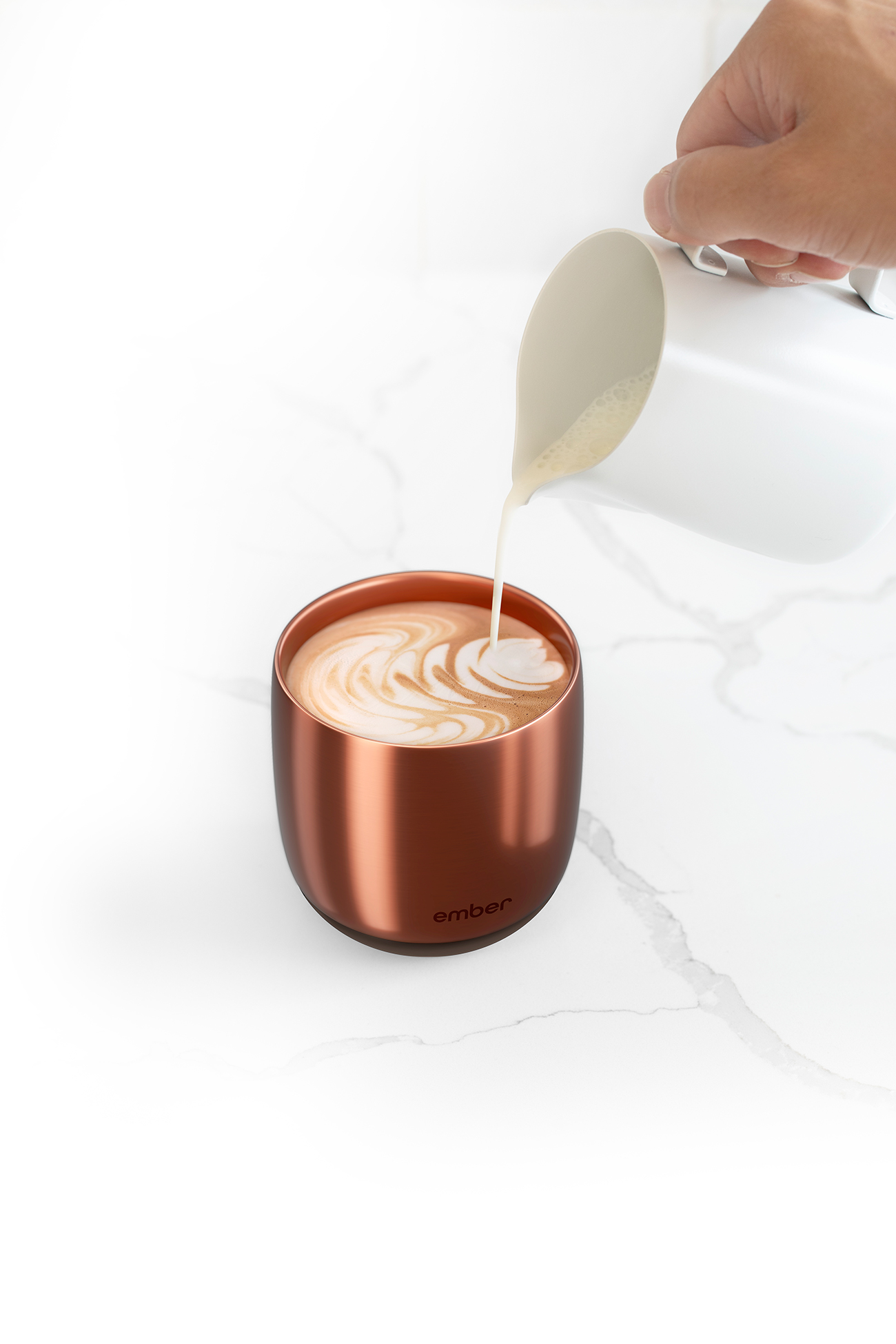 Una tazza da caffè color rame con latte art, che viene riempita di latte da una lattiera.