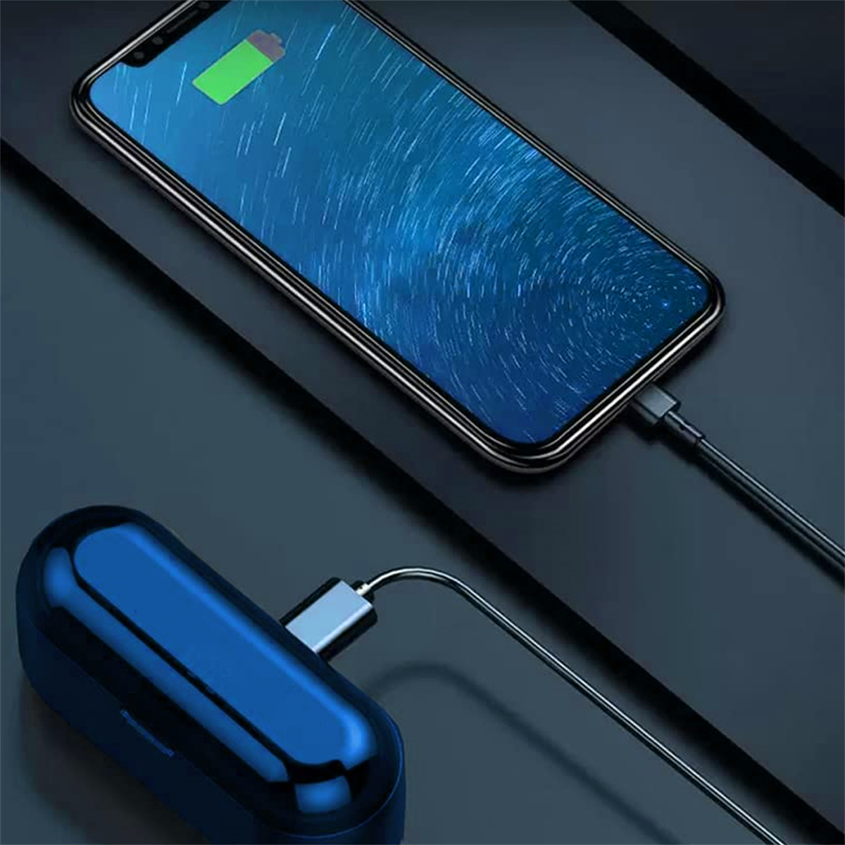 Ein Telefon wird geladen, mit einem blauen Kopfhörer-Etui verbunden, auf einer dunklen Oberfläche.