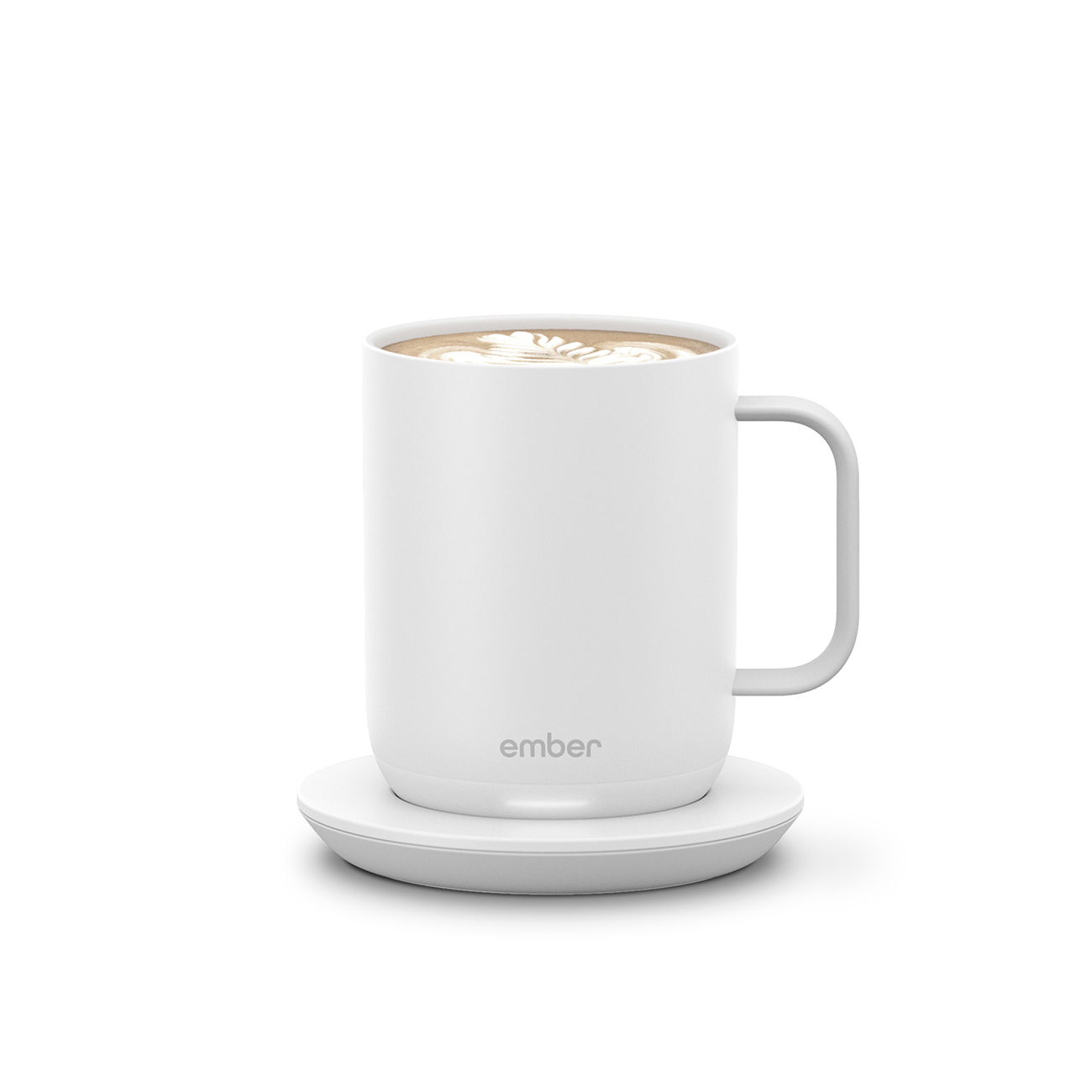 Una tazza bianca con manico, piena di caffè e latte art, posta su un sottobicchiere bianco.
