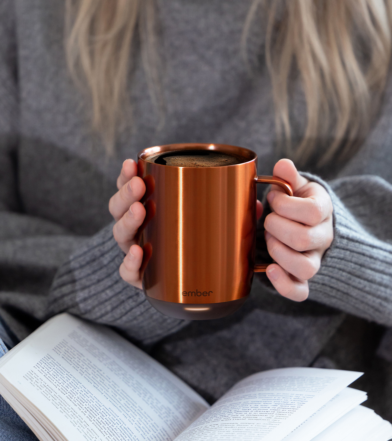 Una persona che tiene una tazza da caffè color rame, con un libro aperto in primo piano.