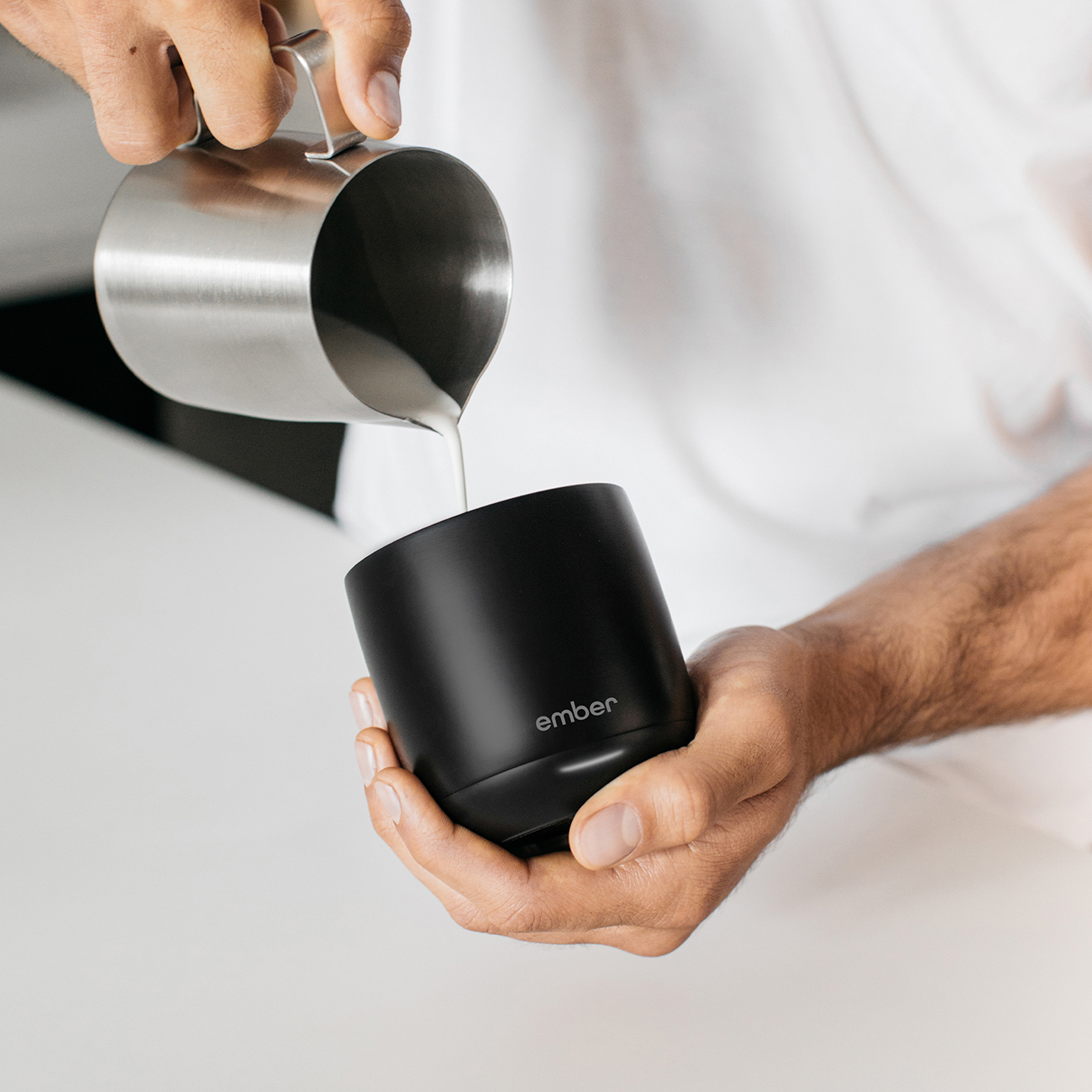 Una persona versa del liquido in una tazza nera con la scritta 'ember'. Il liquido sembra essere latte.