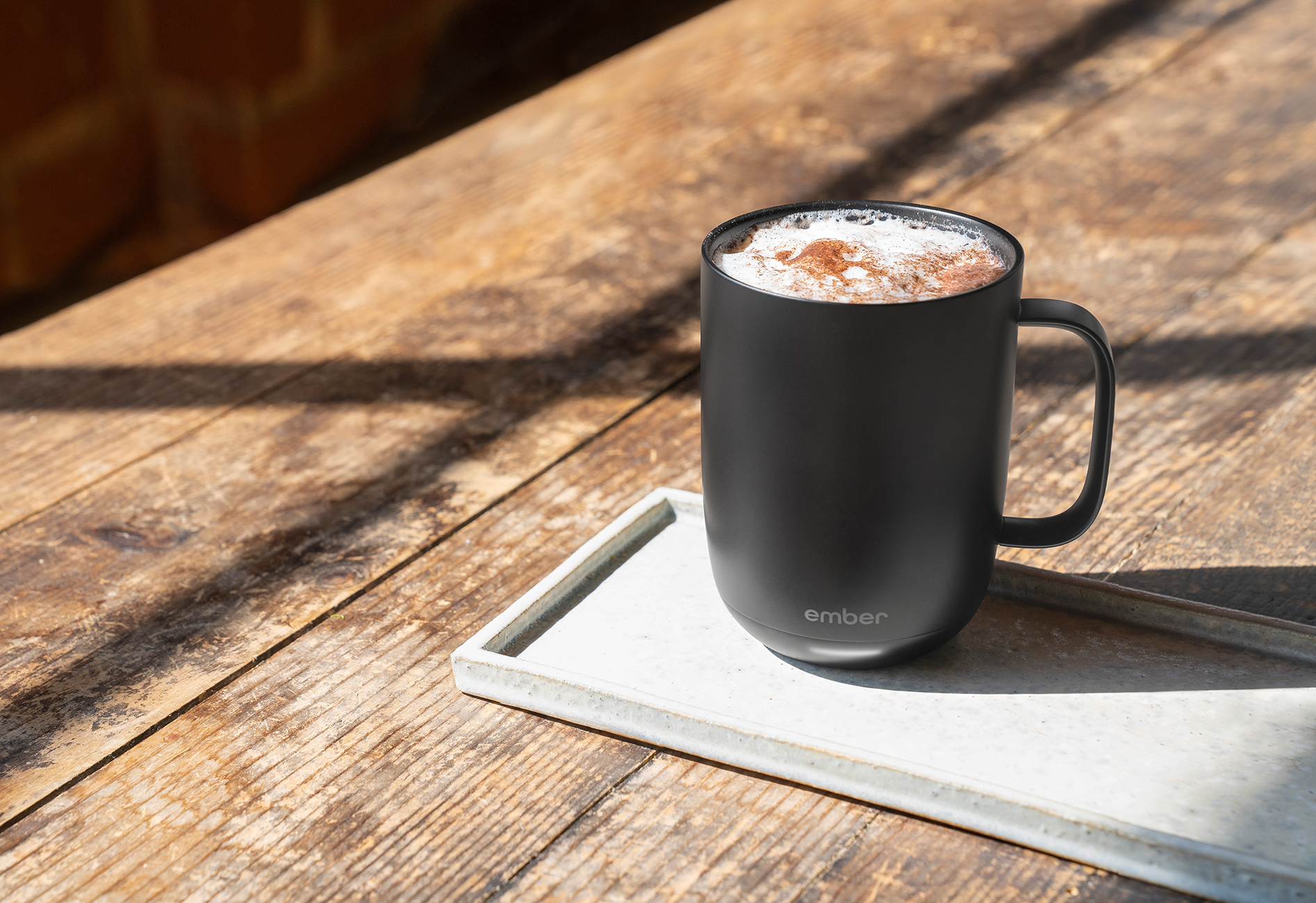 Una tazza nera con caffè e schiuma su un tavolo di legno, su un vassoio bianco.