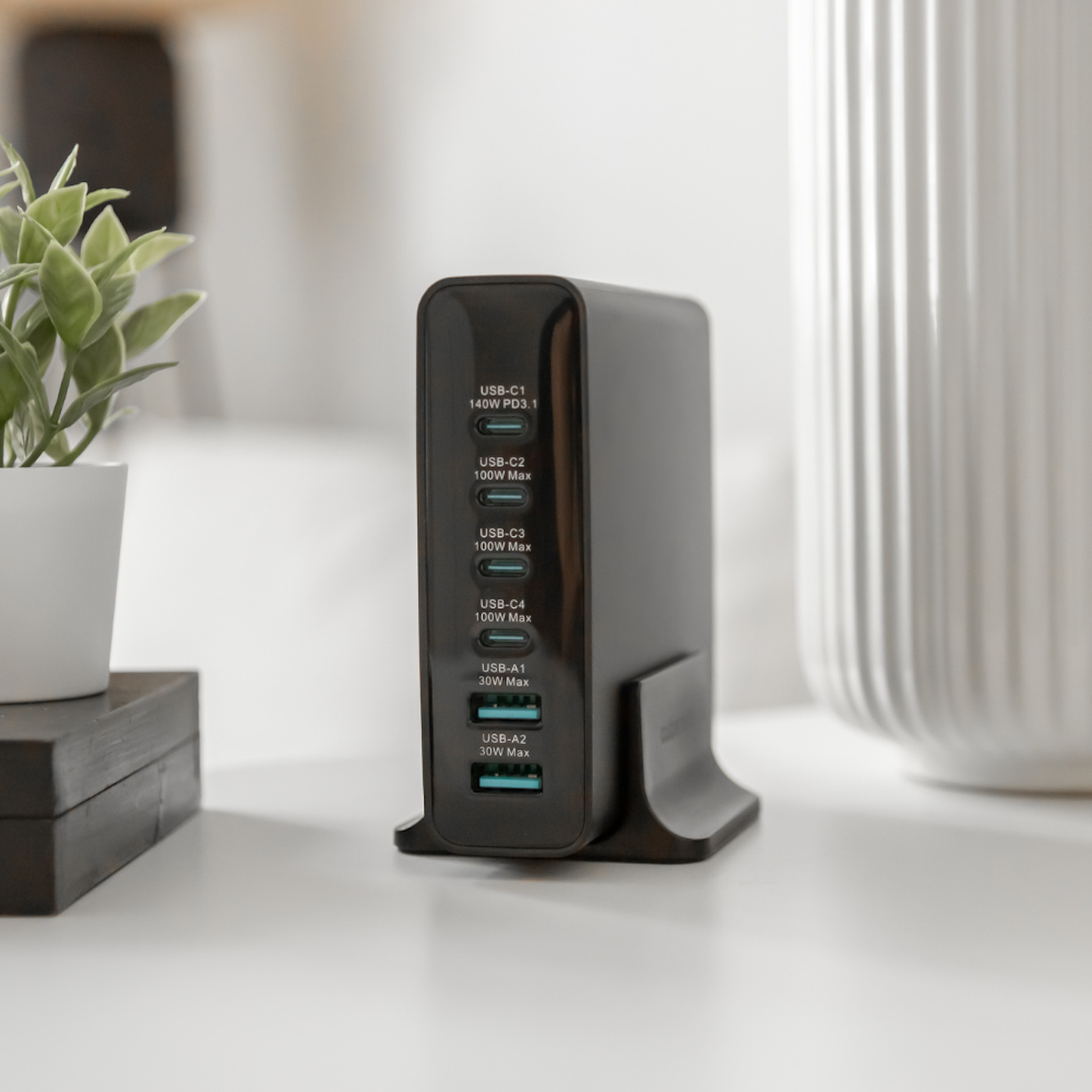Adattatore di alimentazione nero con più porte USB. Un vaso bianco e una pianta sullo sfondo.